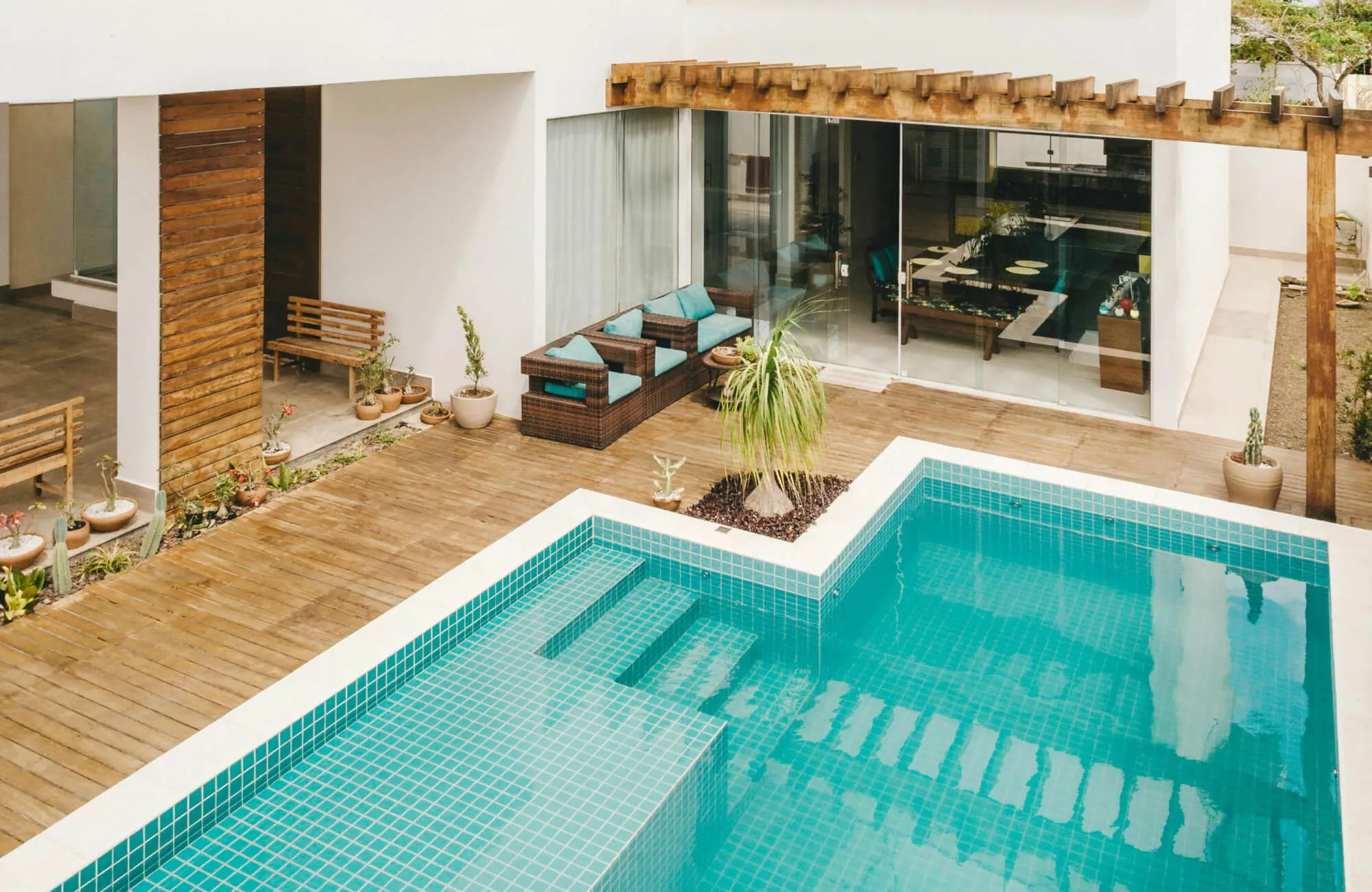 Modern outdoor pool with turquoise mosaic pool tile, blending seamlessly with wooden decking and cozy rattan seating for a stylish and relaxing retreat.