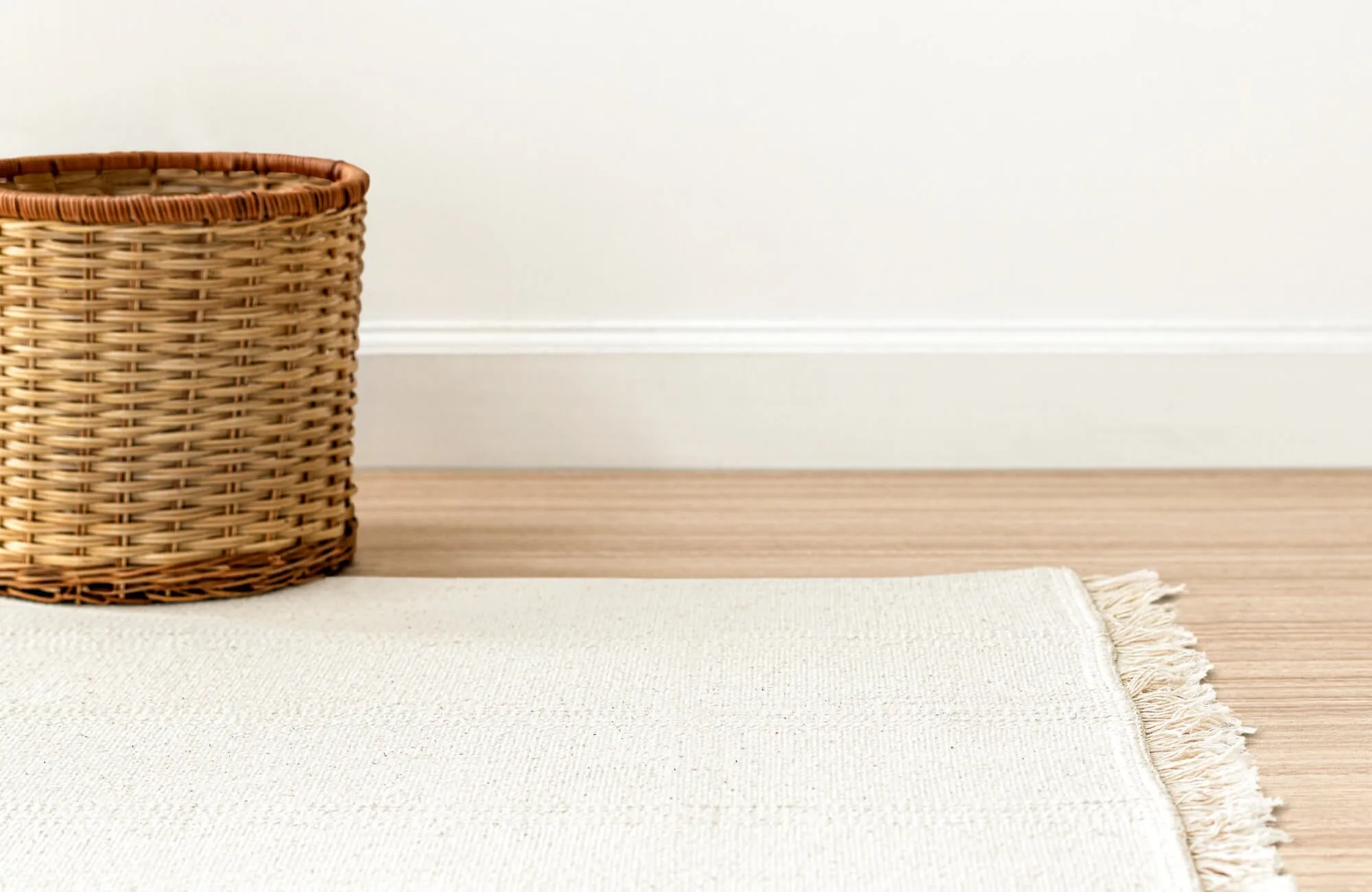 Light-colored rug with woven texture beside a wicker basket on a wood floor, creating a clean, minimal look.