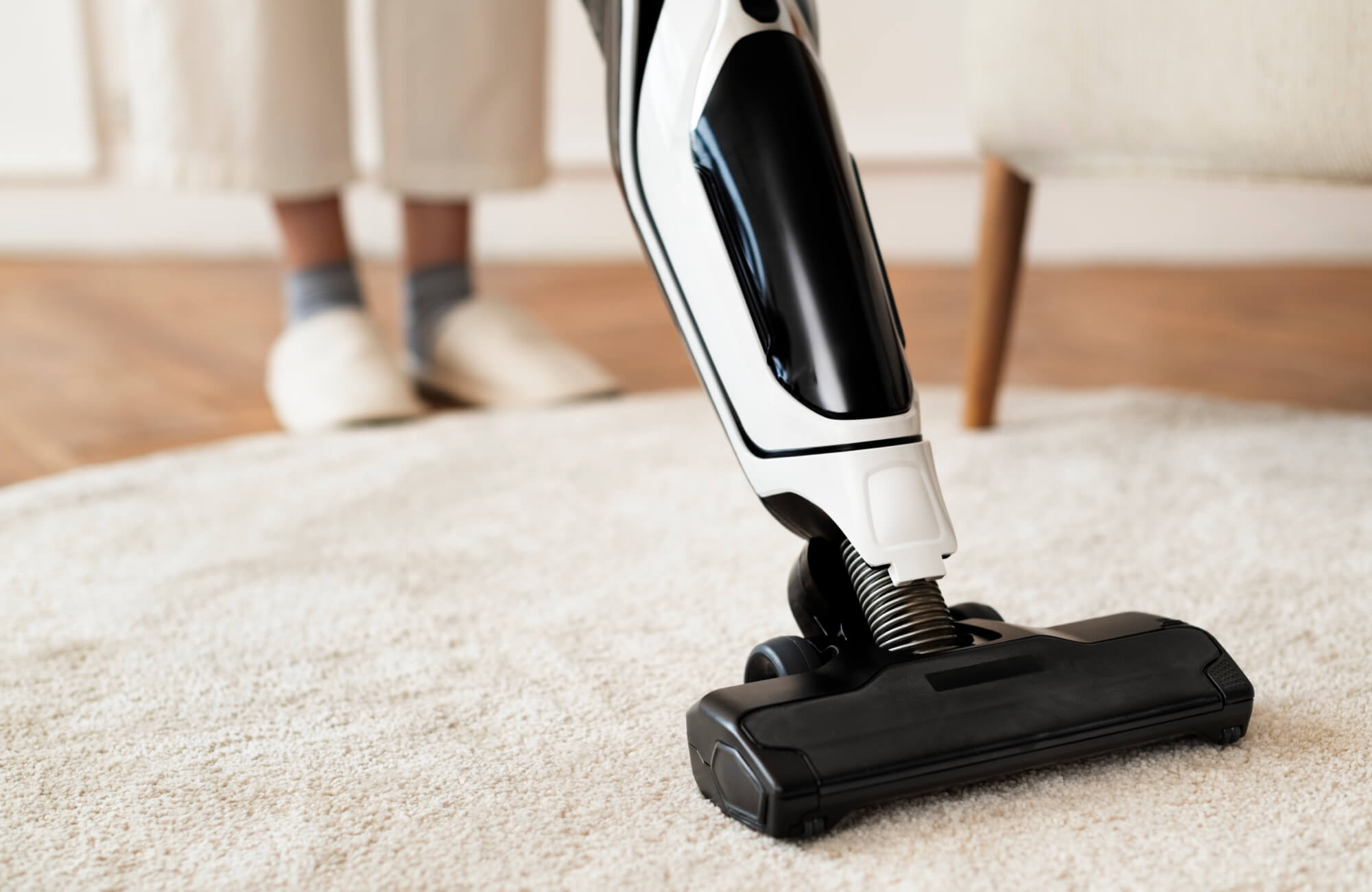 null A Person vacuuming a light rug with a handheld vacuum cleaner to maintain cleanliness and extend rug life.