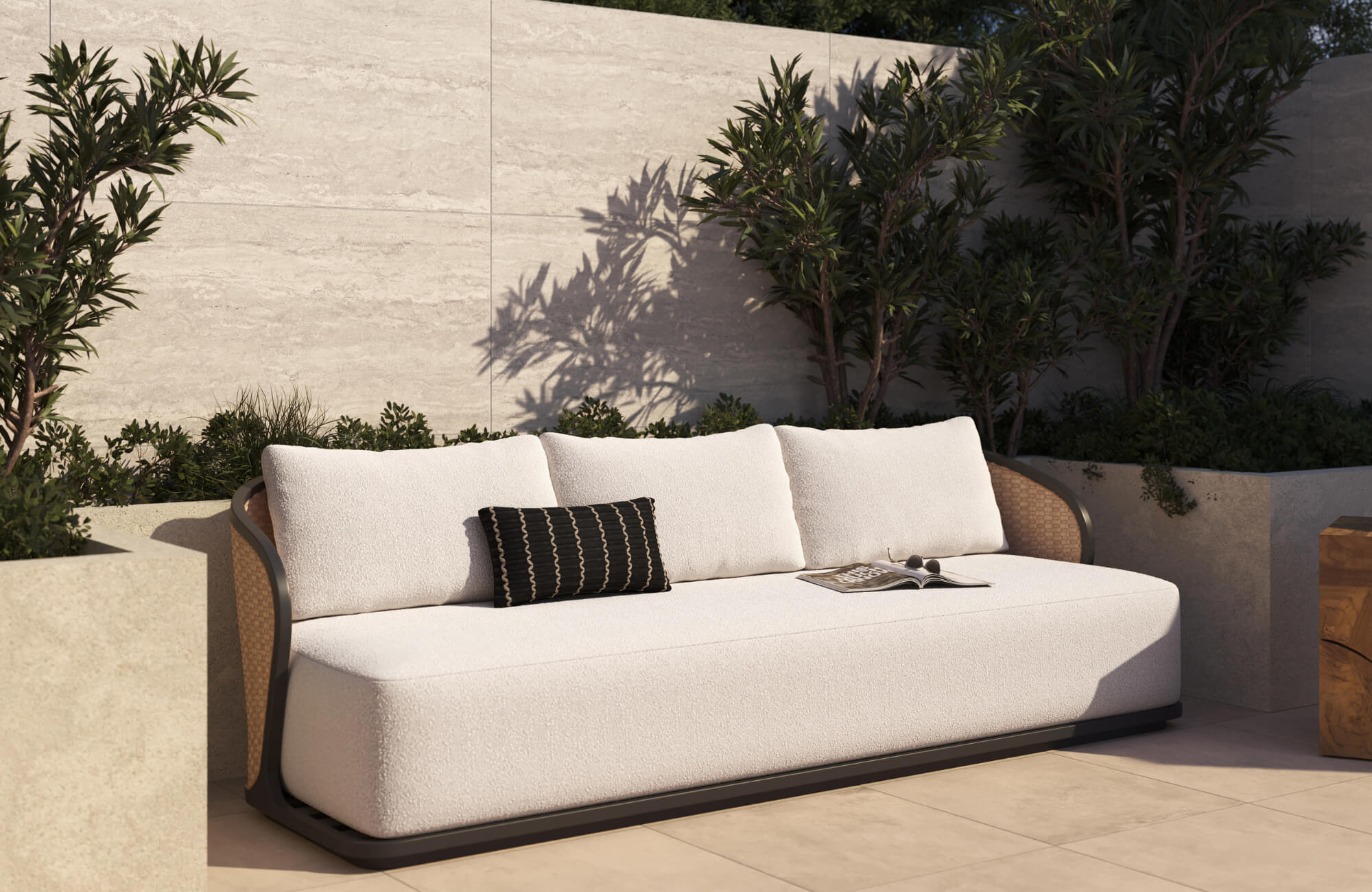 Black lumbar pillow styled on a curved white outdoor sofa beside stone walls and landscaped greenery.