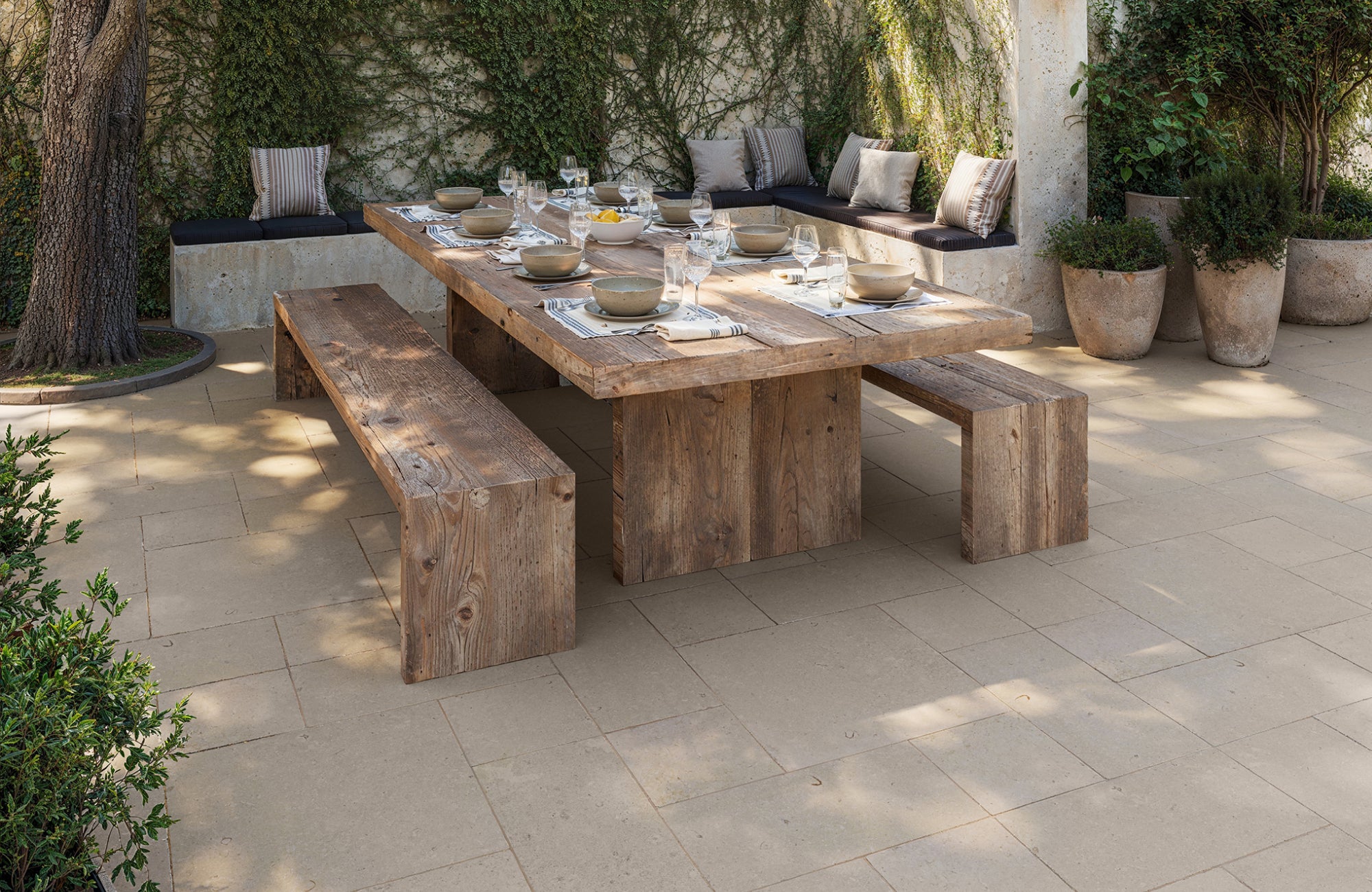 Outdoor porcelain pavers under a rustic dining setup, showcasing textured surface and warm tones in sunshine.