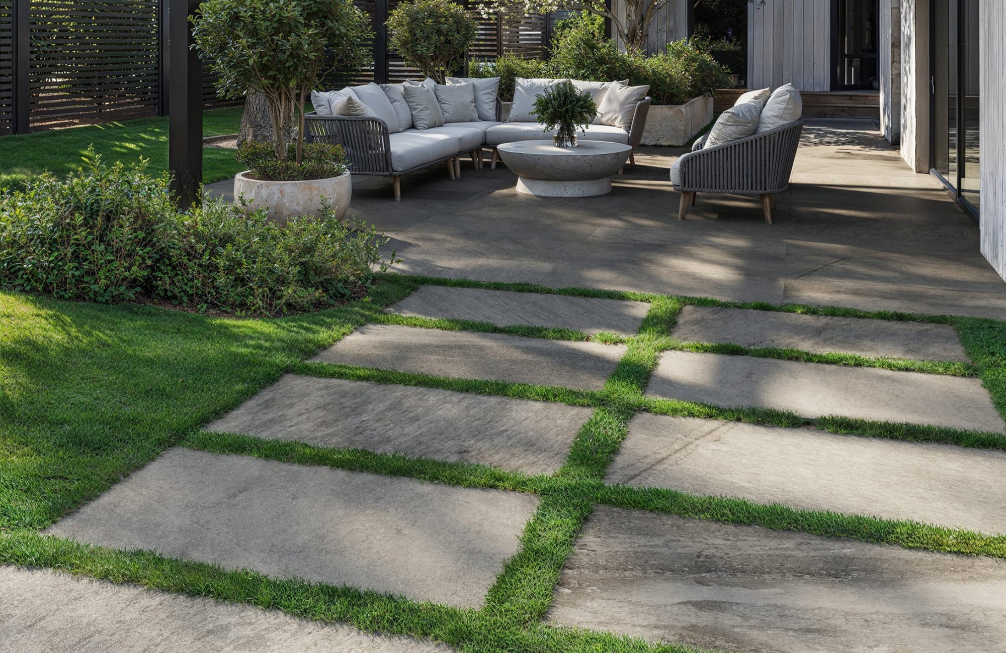 Outdoor porcelain paver tiles arranged in grass-lined grids, creating a durable, modern patio edge around a seating area.