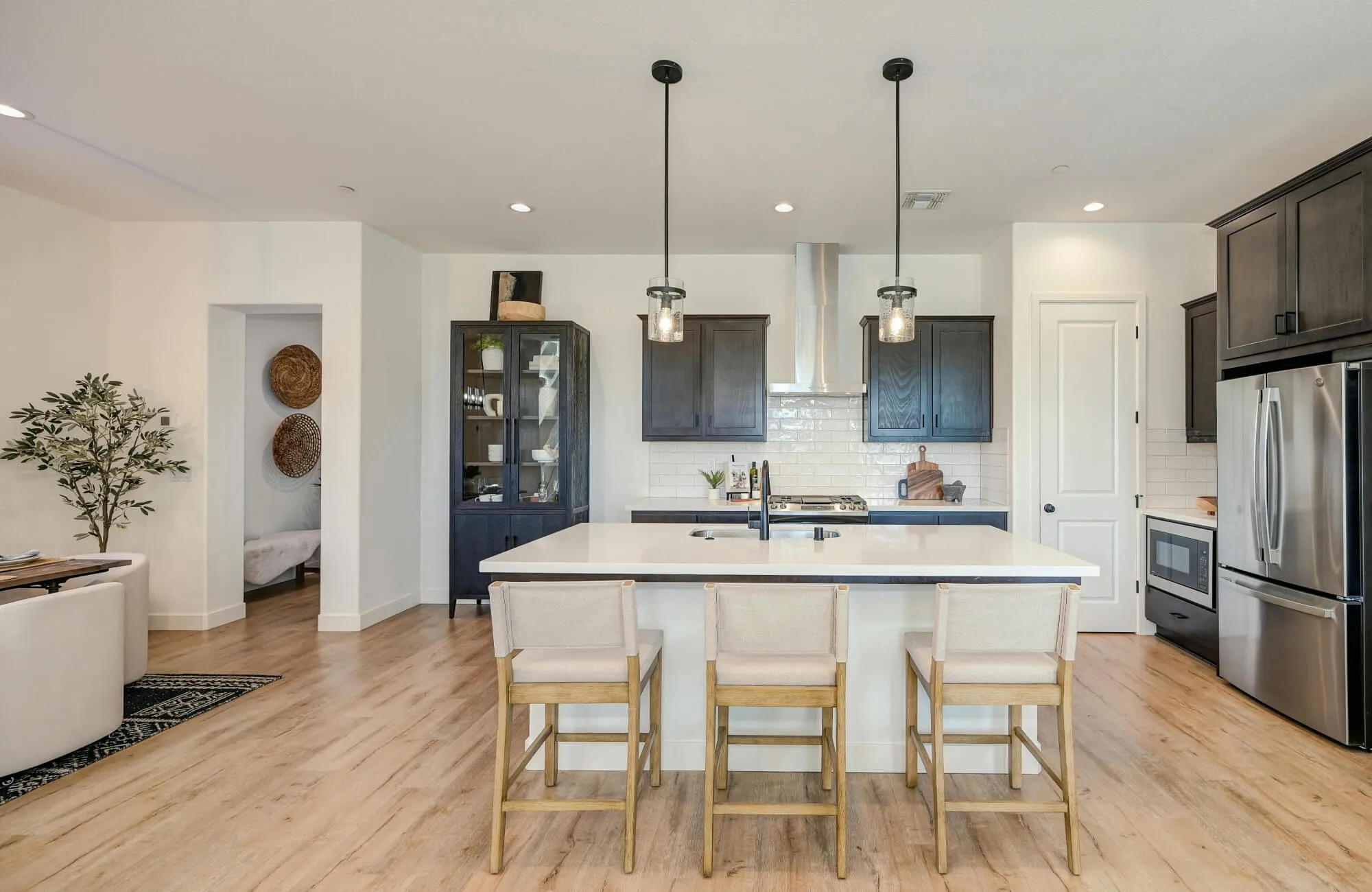 Black metal pendants hang above a bright kitchen island with light wood floors and upholstered stools.