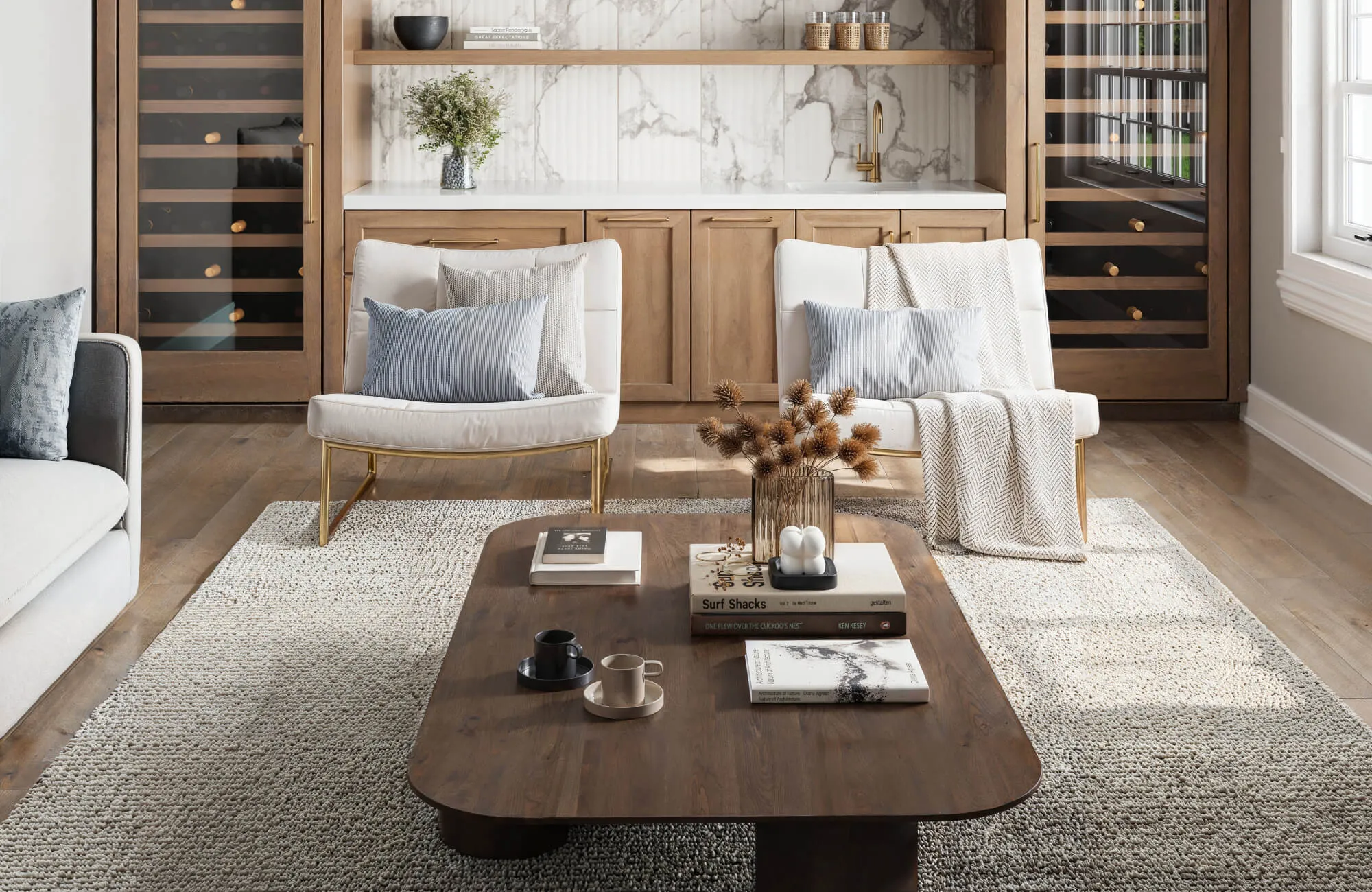Modern living room with cozy seating, a rich wood coffee table, and a textured neutral rug complementing the marble-accented wet bar and wine storage.