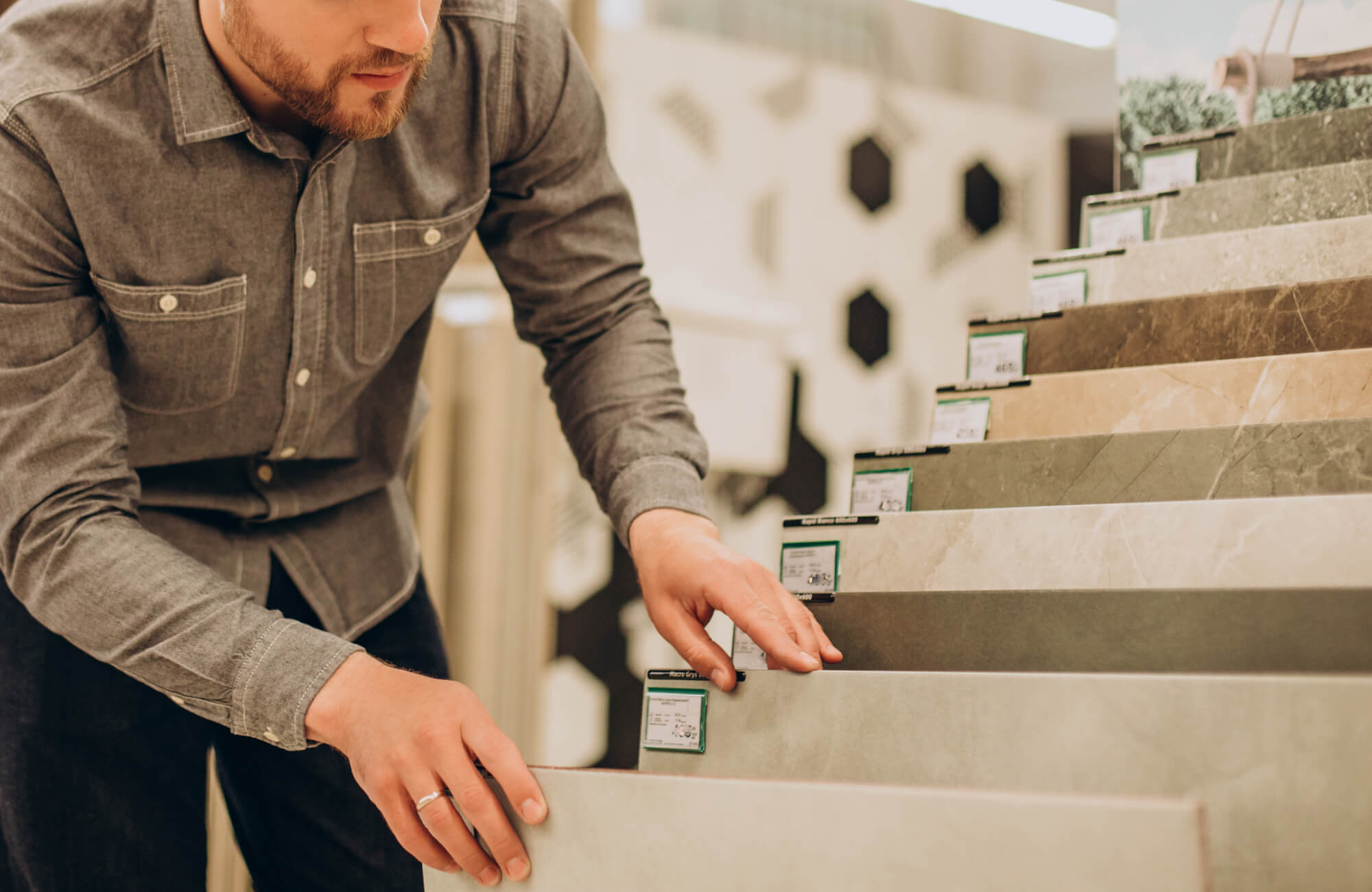 Man comparing neutral-toned tile samples in a showroom, exploring options for bathroom or flooring design.
