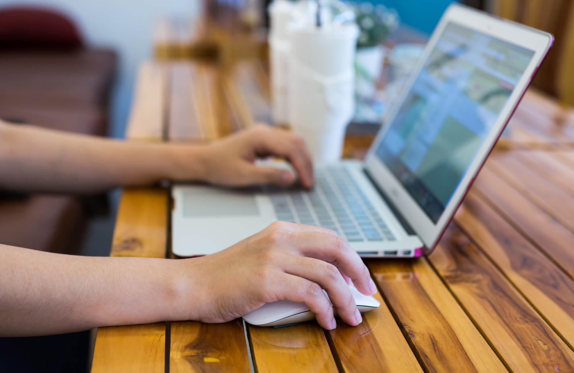 Close-up of a person using a laptop and mouse on a wooden table, working on a project or creating a mood board.