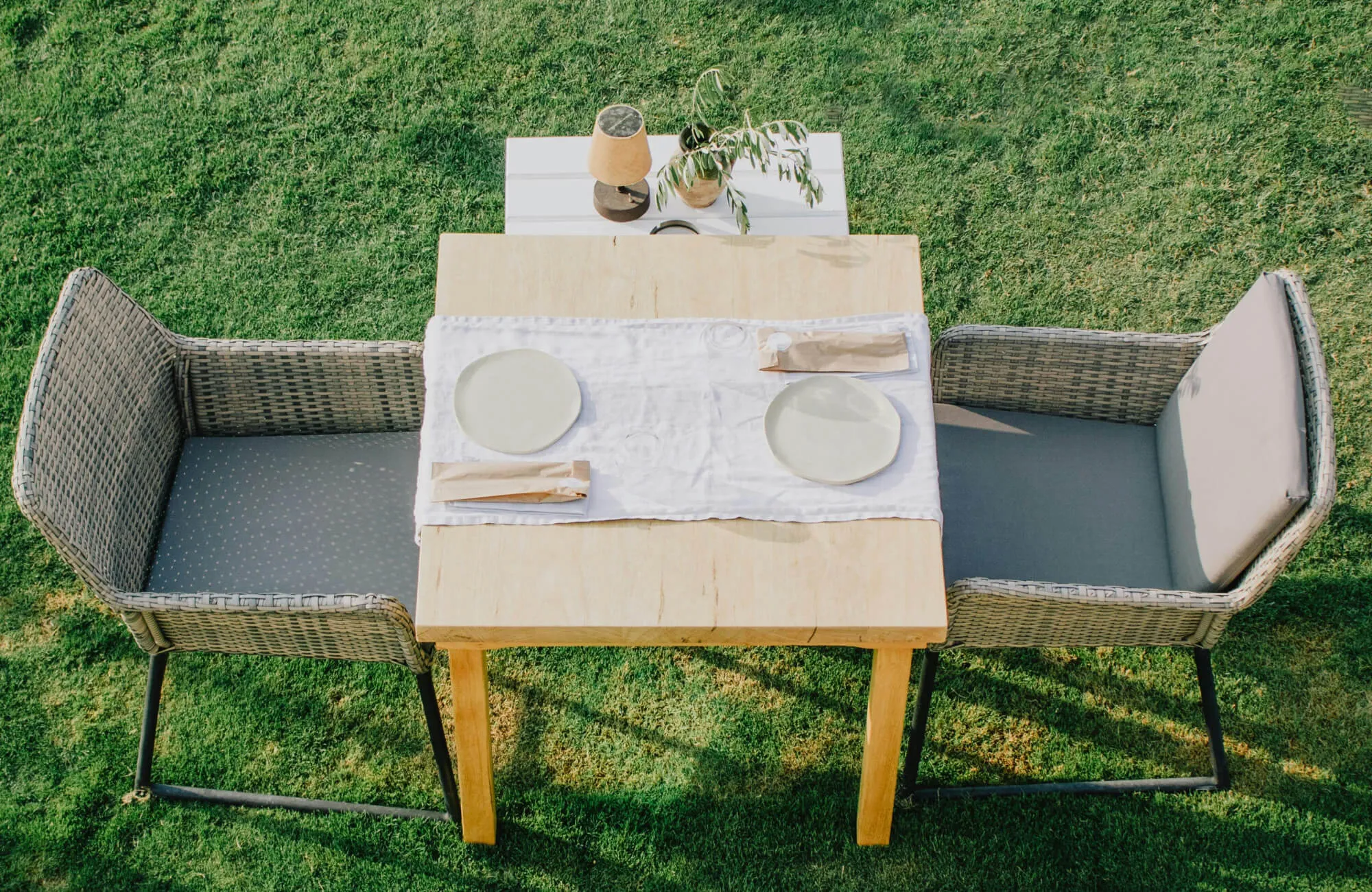 Woven outdoor dining chairs with cushioned seats arranged around a wood table on a grassy lawn, creating a relaxed, weather-ready setup for open-air meals.