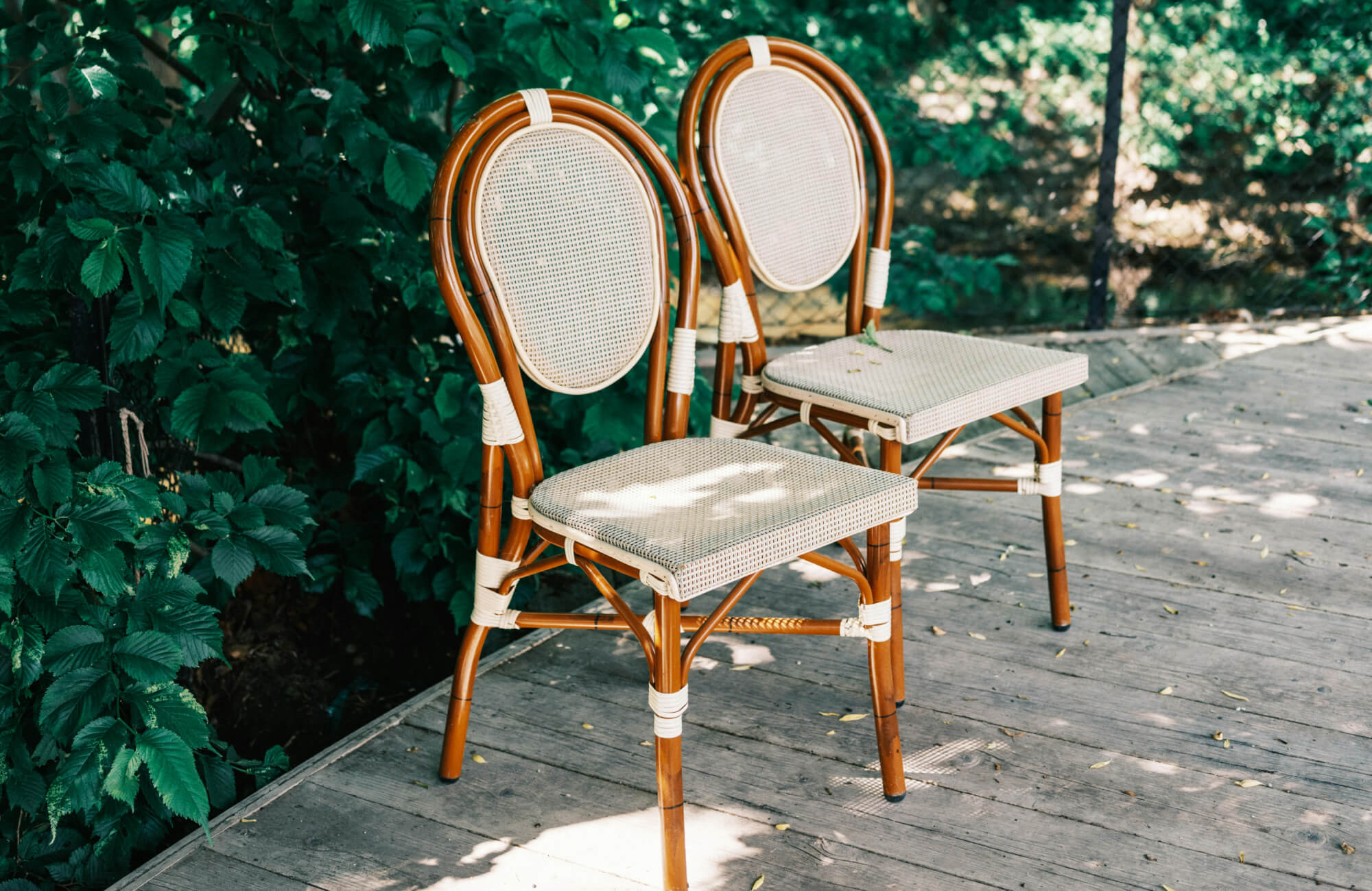 Outdoor dining chairs featuring woven seats and rounded wood frames, styled on a deck and surrounded by leafy plants for a relaxed, nature-focused setting.