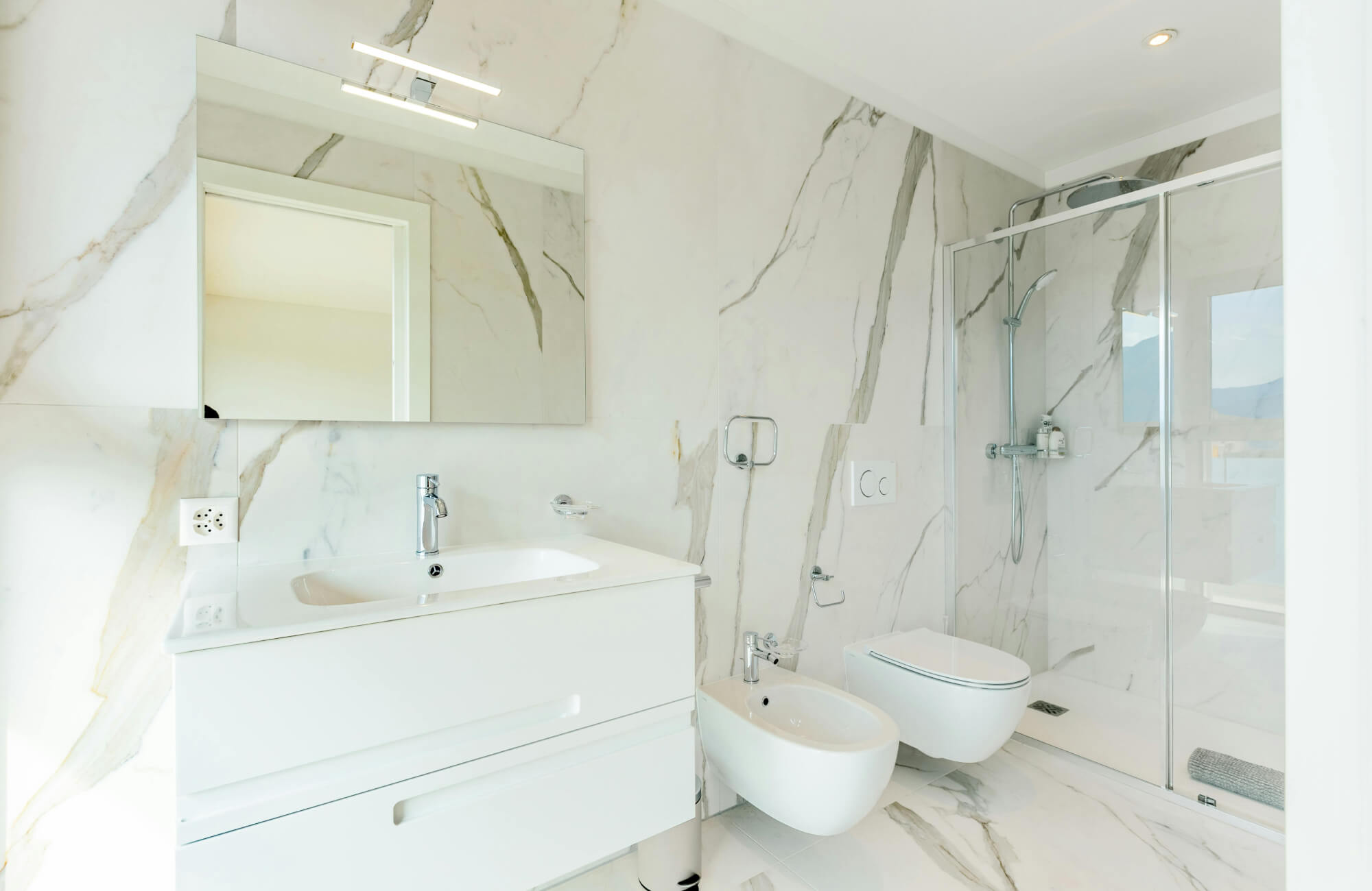 null Contemporary bathroom design featuring marble-style walls and floors, a frameless glass shower, and minimal white fixtures with integrated lighting.