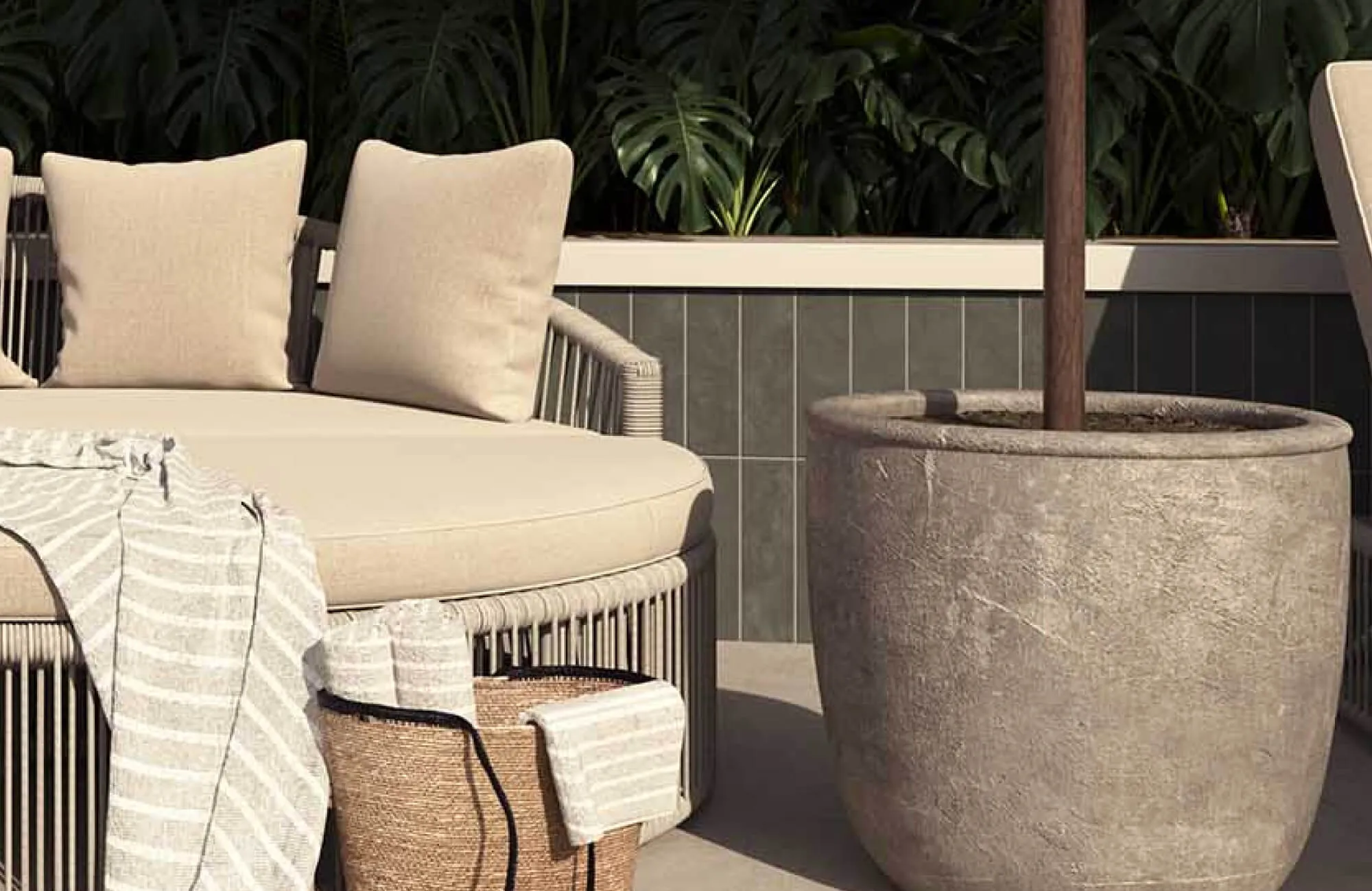 A serene outdoor lounge features cream-upholstered seating, woven detailing, a textured planter, and layered neutral textiles framed by lush tropical greenery.
