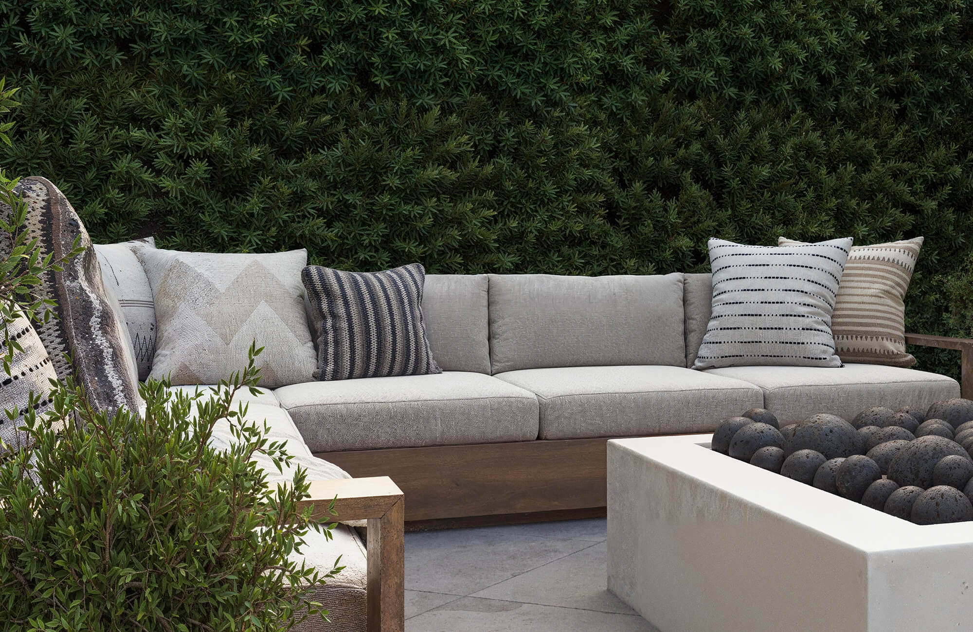 null Patterned accent cushions are arranged across a deep outdoor sectional surrounded by dense greenery and durable hardscape materials designed for everyday use.