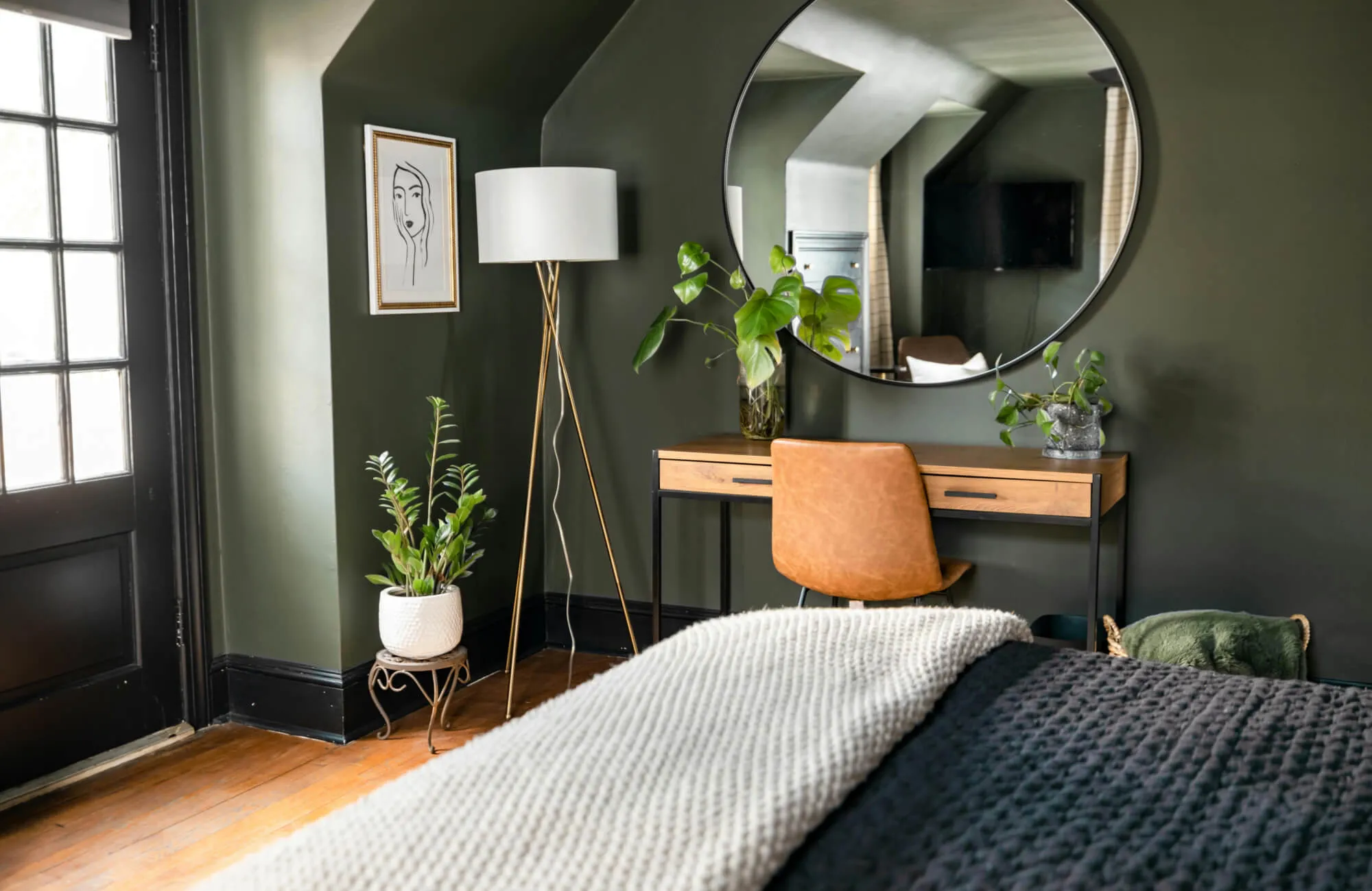 Cozy bedroom with a round mirror above a wooden vanity and plants adding a natural touch to the modern space.