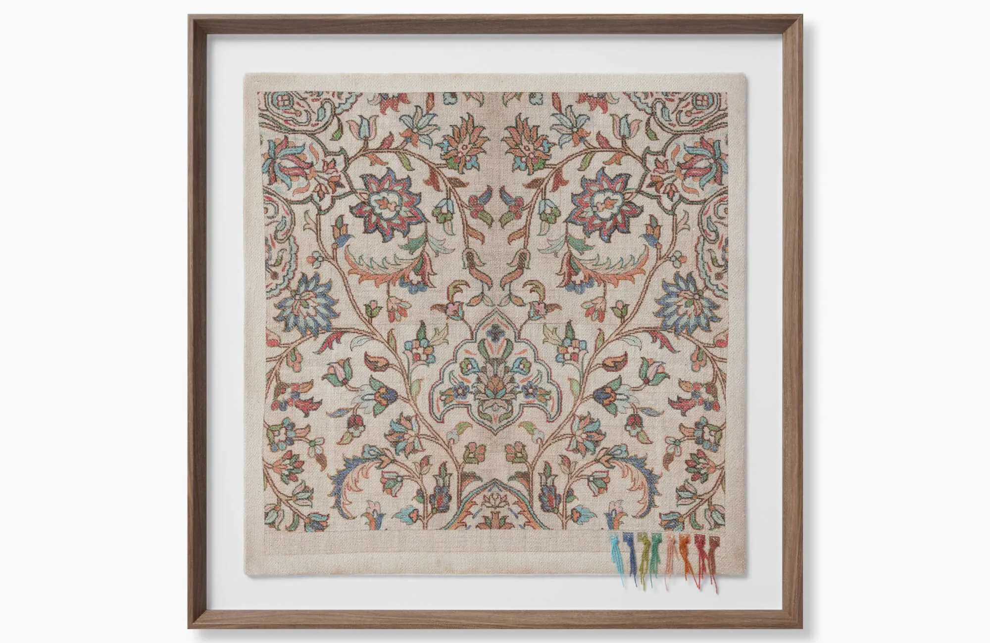 Framed textile wall art with a floral pattern, muted blue, coral, green, and beige embroidery, and a warm wood frame against a white background.