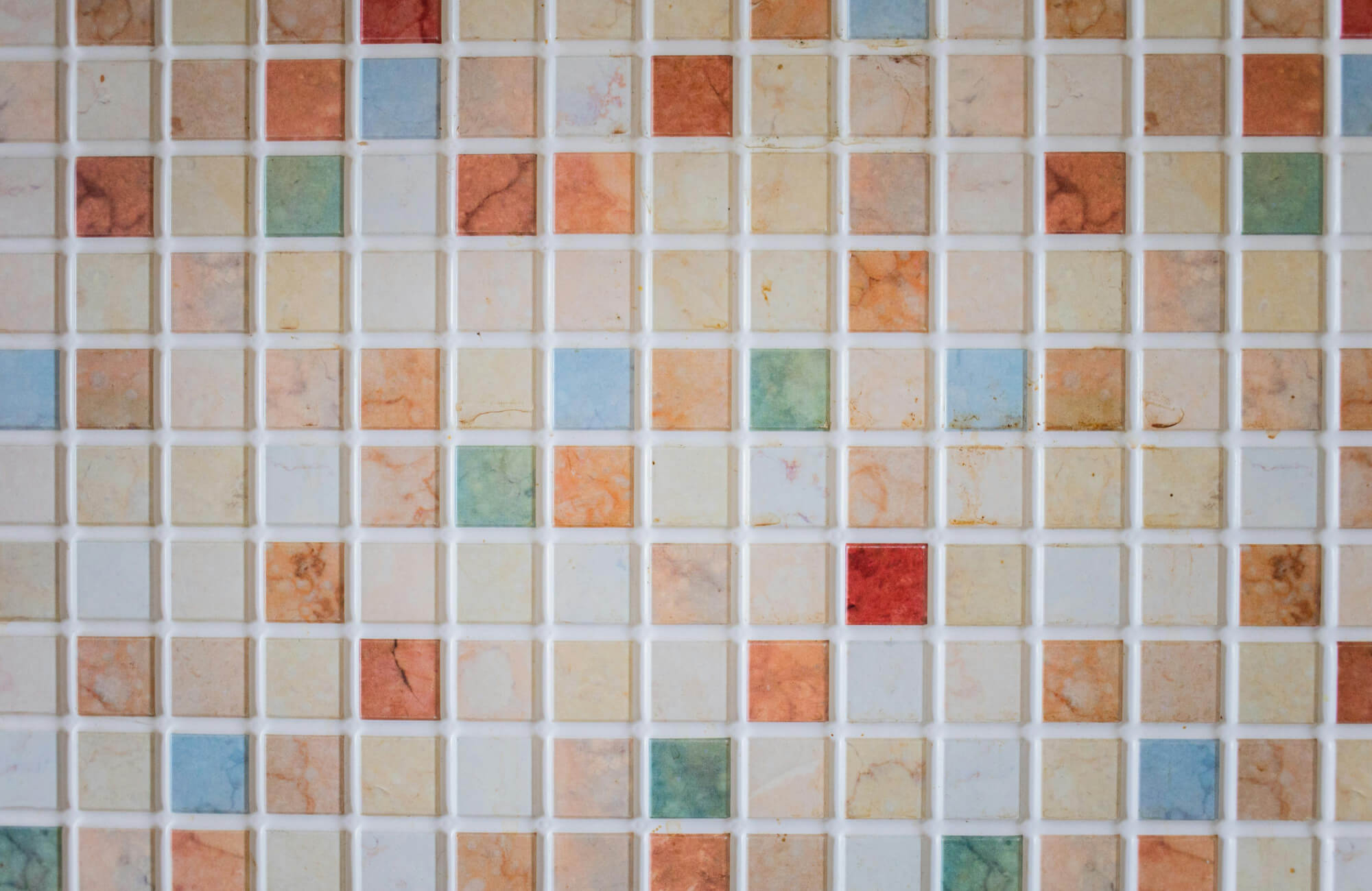 null Close-up of multicolored square mosaic tiles in orange, cream, green, blue, and red shades with visible grout lines.