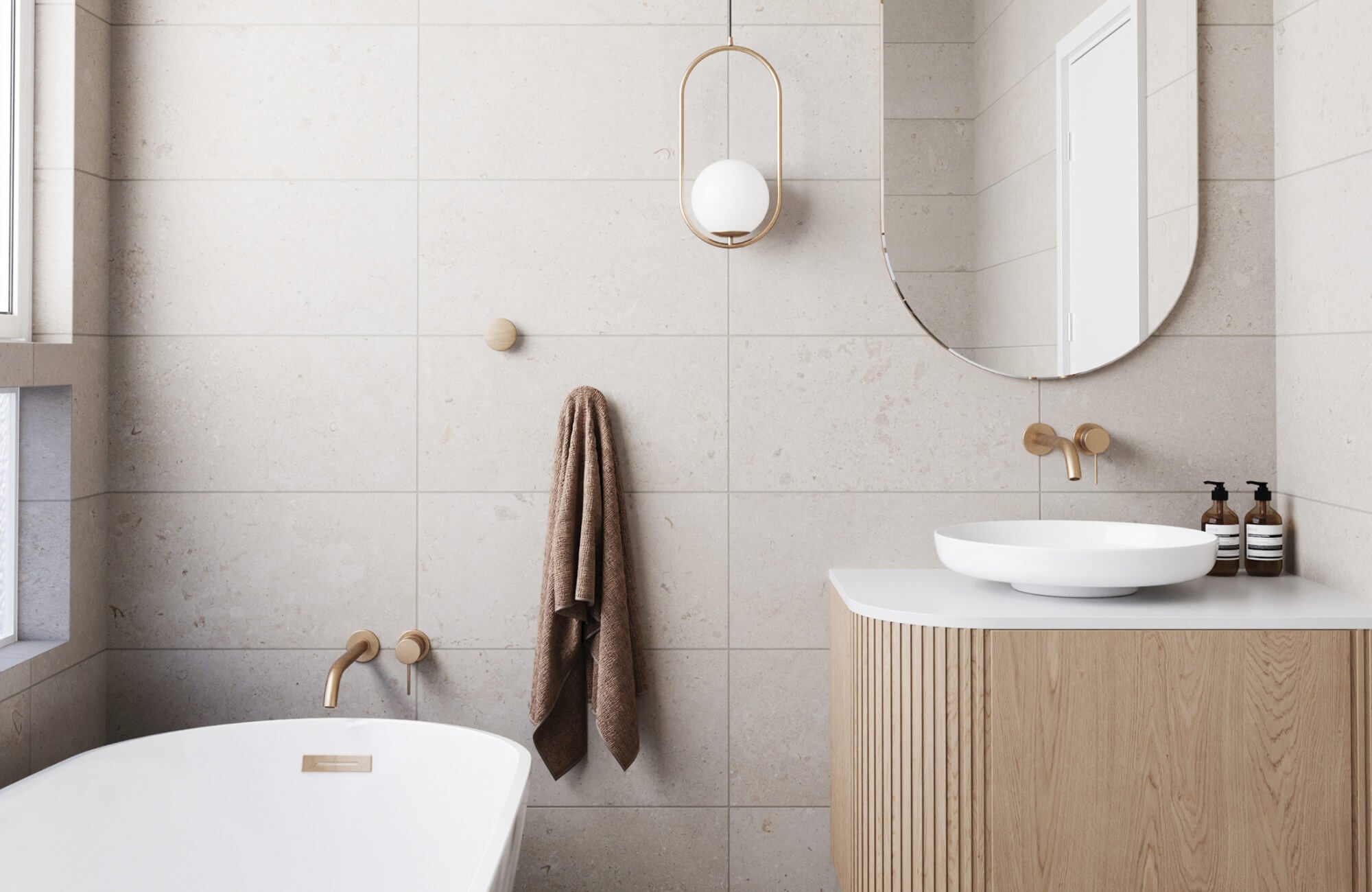 Minimalist bathroom featuring a soft beige base with brown speckled stone look tiles, a freestanding white tub, natural wood cabinetry, and brushed gold fixtures for a serene, modern retreat.