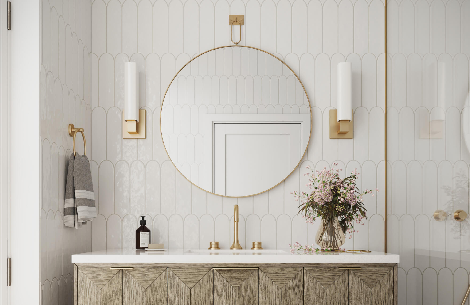 Modern vanity setup featuring a circular mirror, gold-accented lighting, scalloped white tiles, and a natural wood cabinet with soft floral decor.