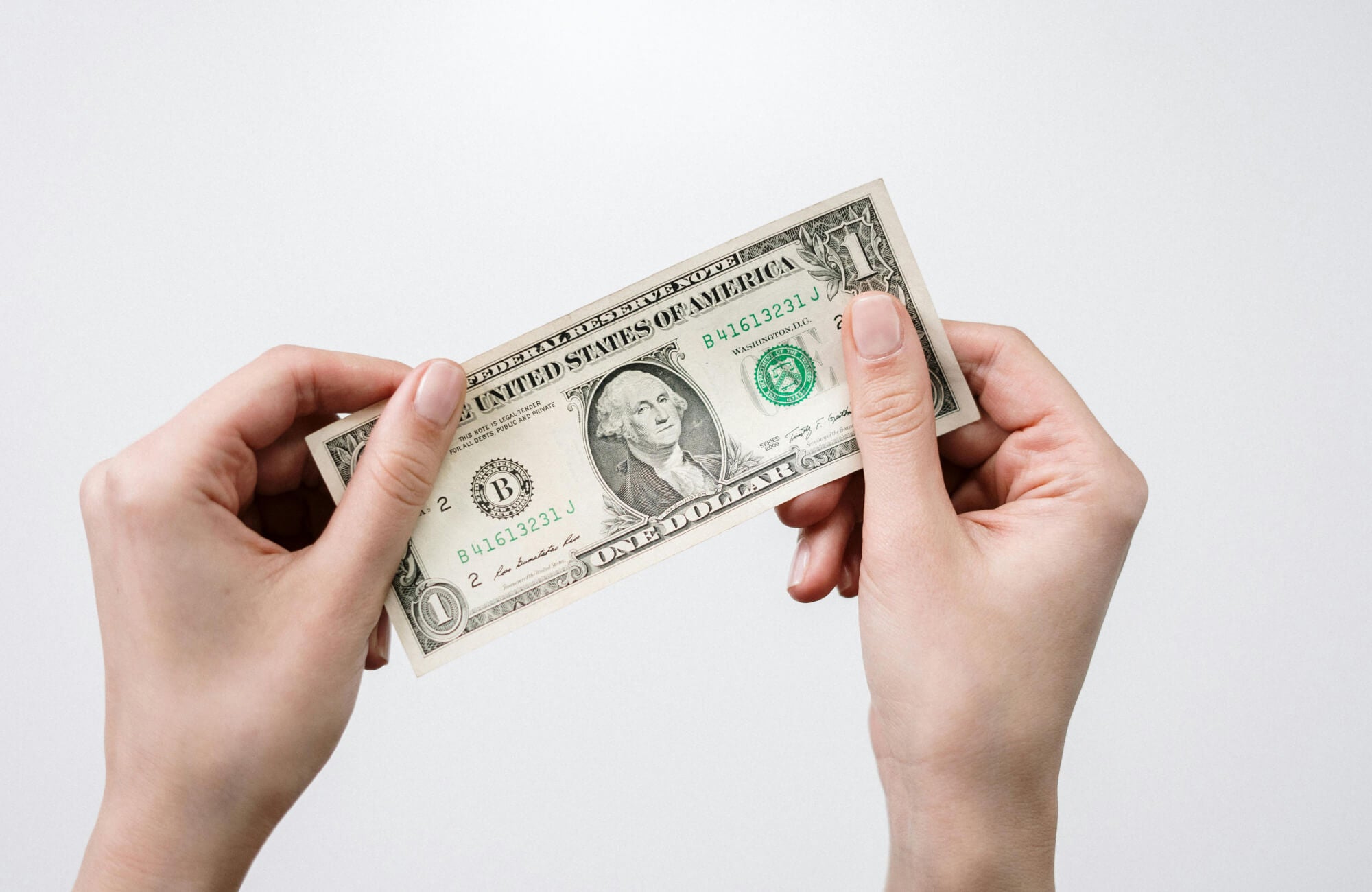 Close-up of two hands holding a one-dollar bill against a white background.