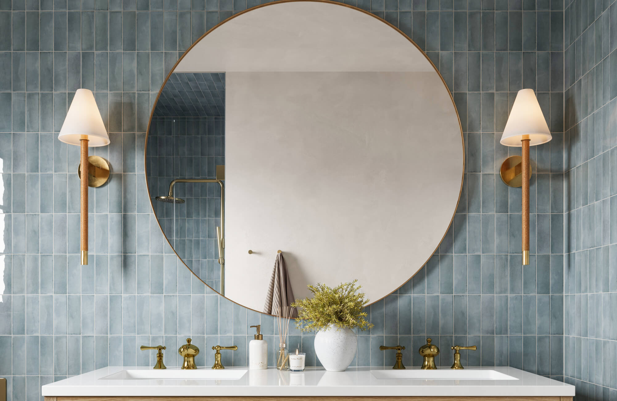 Elegant bathroom vanity with blue tiled walls, a large circular mirror, and gold-accented lighting fixtures framing the sink area.