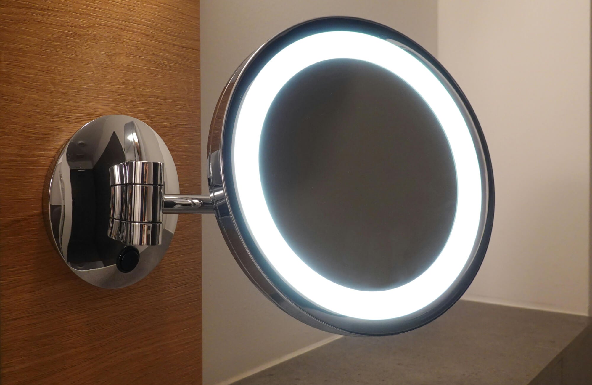 Close-up of a round LED magnifying bathroom mirror with bright halo lighting, mounted on an adjustable chrome arm.