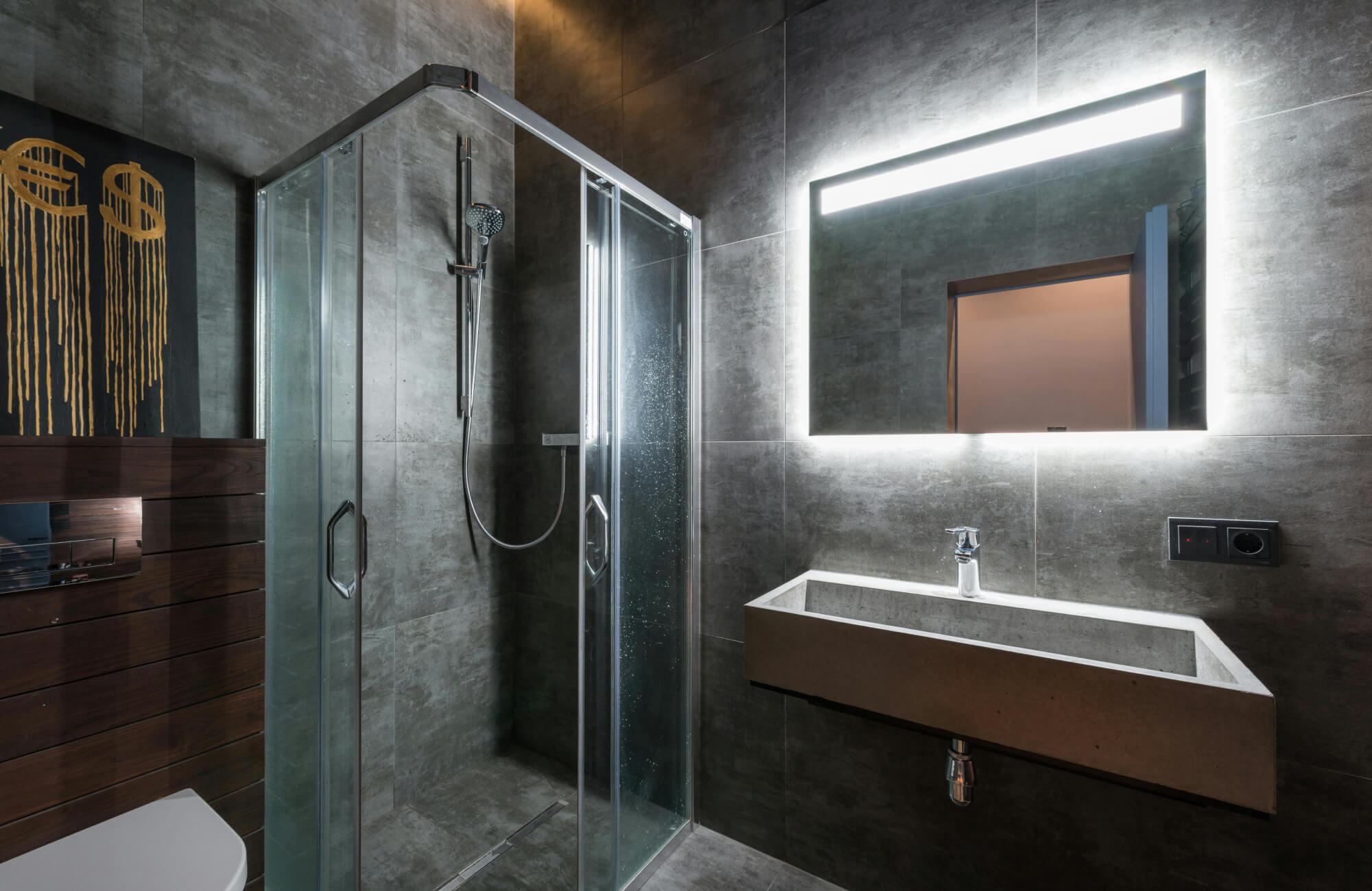Wall-mounted LED bathroom mirror emitting bright perimeter lighting, paired with a minimalist sink and glass shower in a contemporary space.