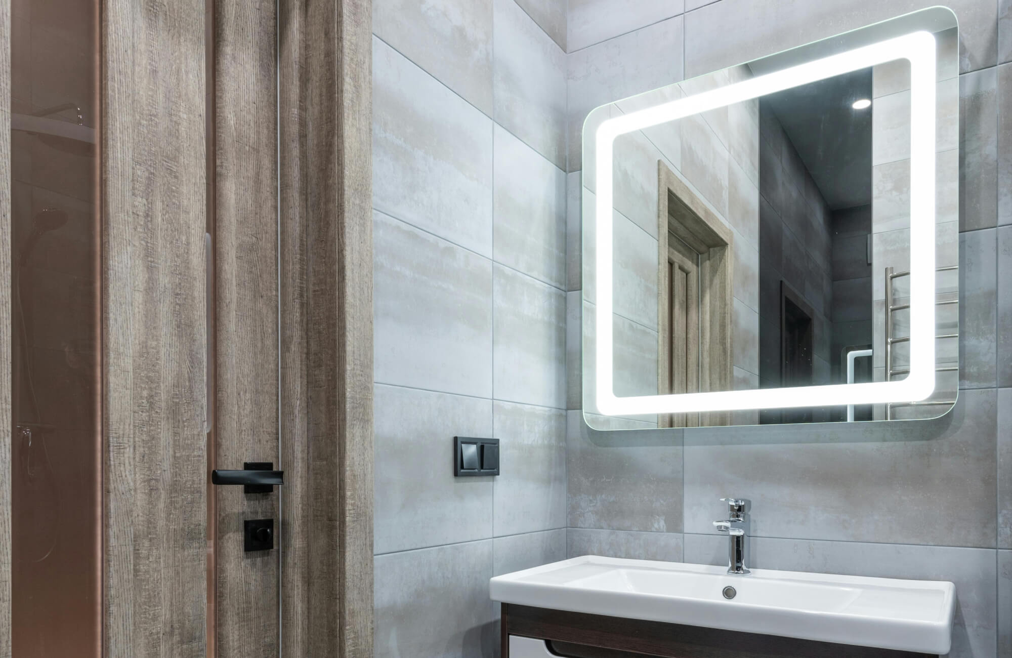 Sleek LED-lit bathroom mirror above a compact vanity, showing how built-in lighting interacts with surrounding tile surfaces.