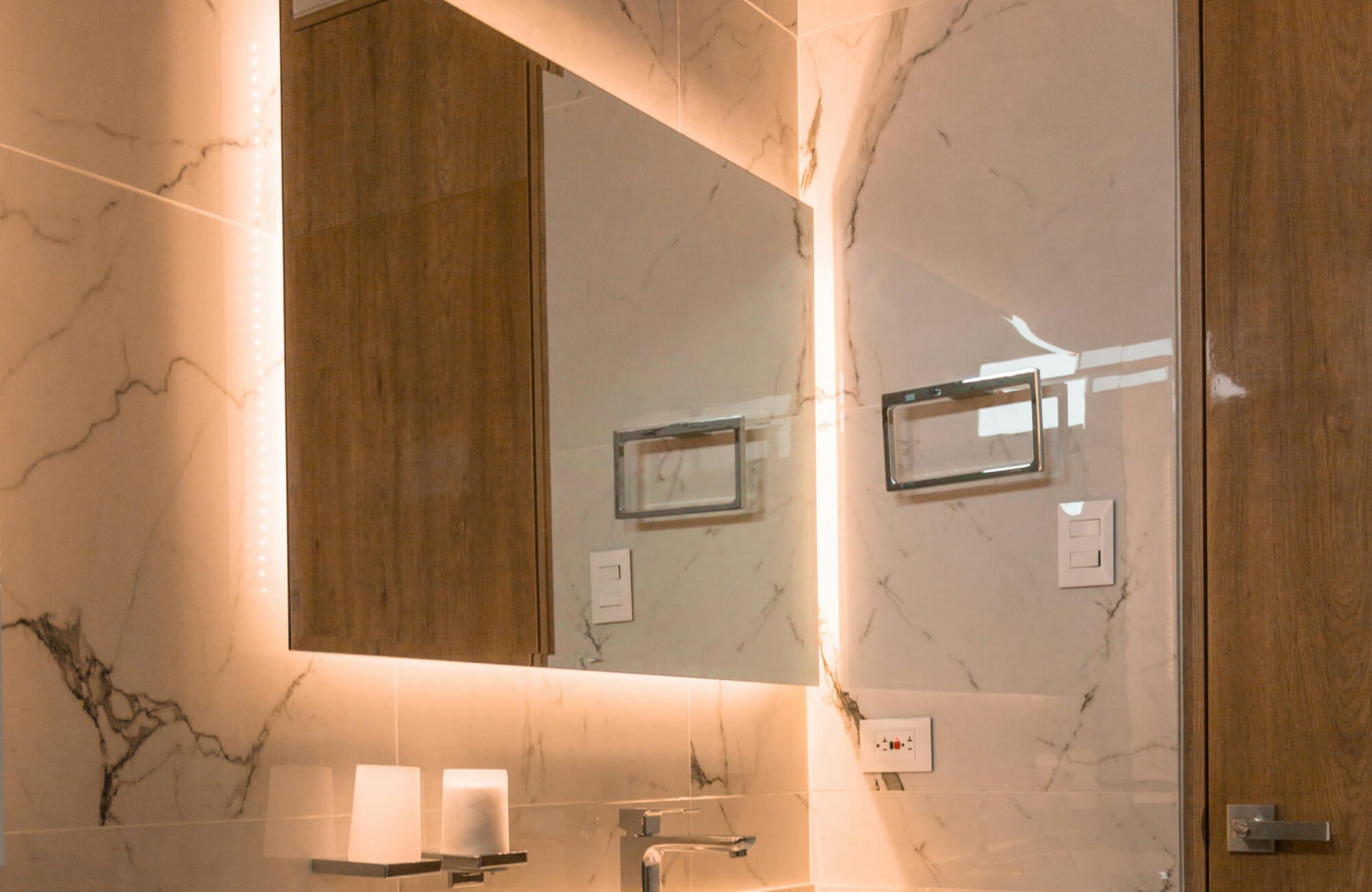 LED bathroom mirror with integrated backlighting mounted over a sink, highlighting how warm LED glow interacts with surrounding cabinetry and stone surfaces.