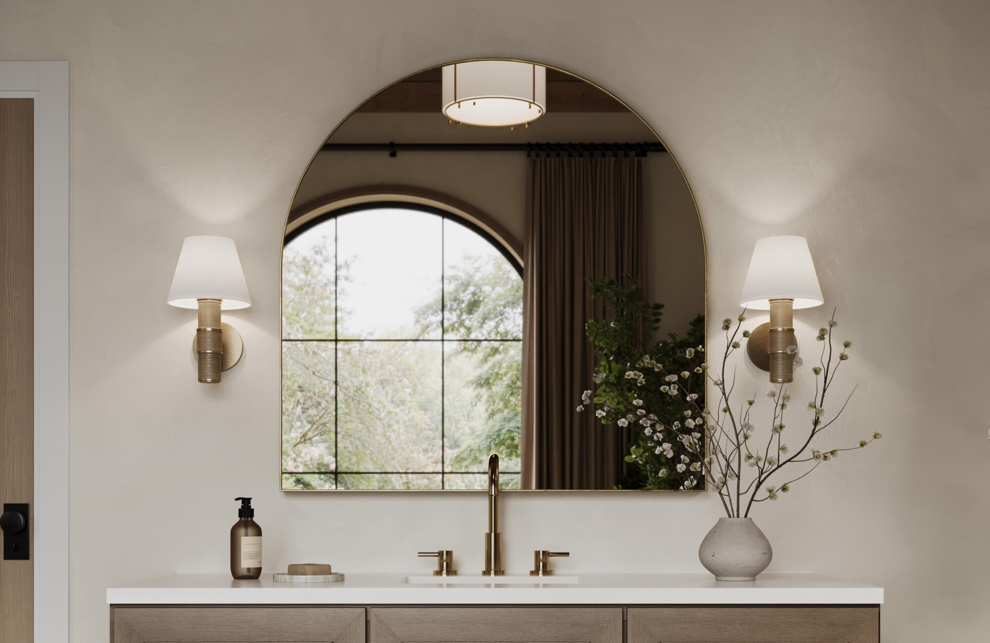 Gold arched wall mirror reflecting natural light, complemented by warm brass fixtures and a clean, minimalist vanity design.