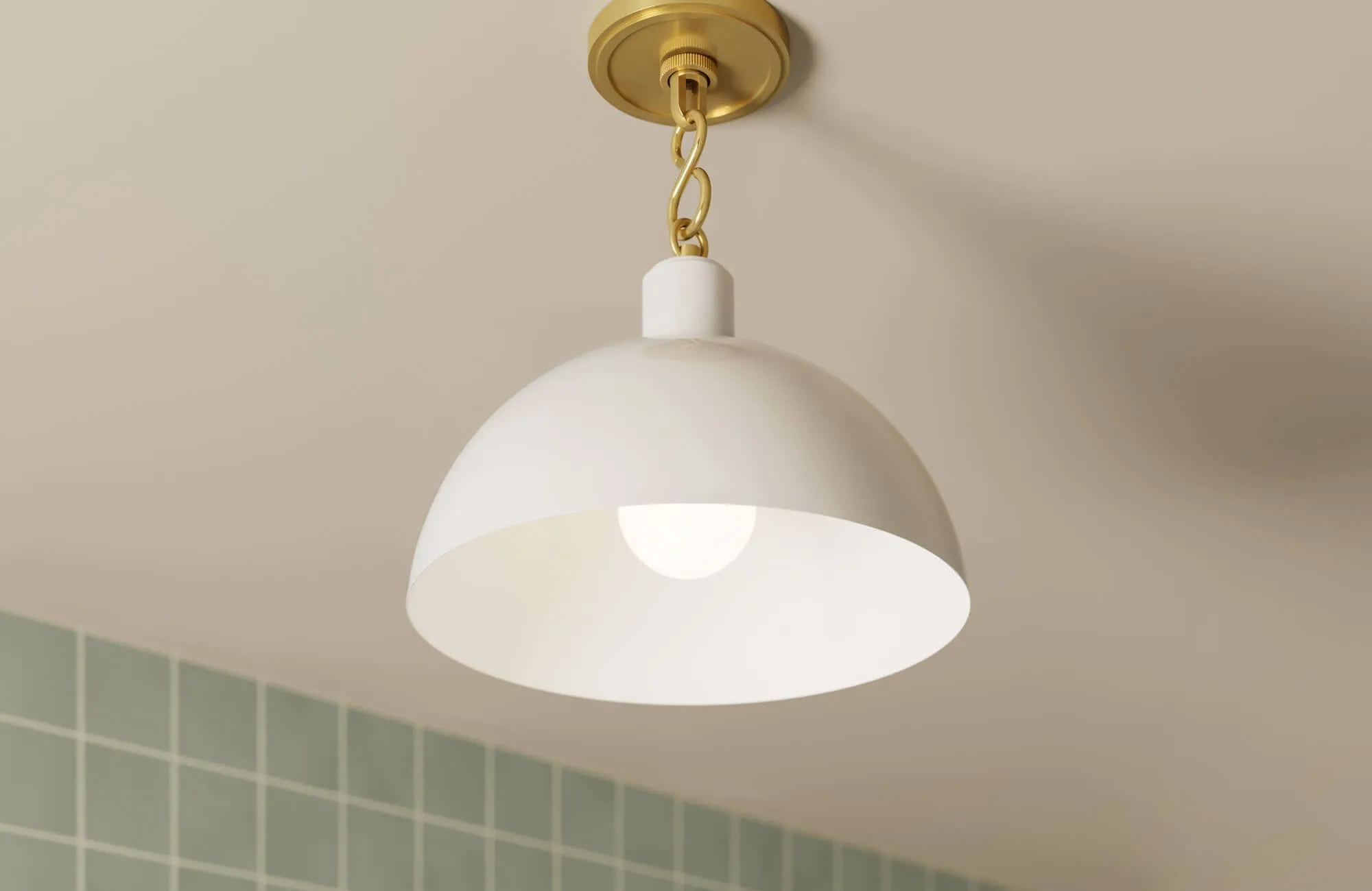 White dome pendant light with a brass chain mount, softly illuminating a space with muted green wall tiles in the background.