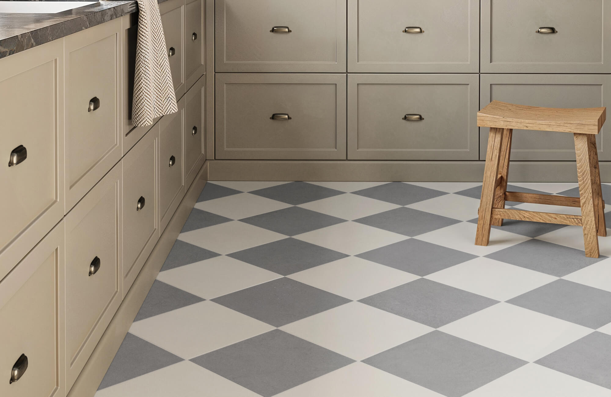 Grey and white checkerboard tile flooring in a soft-toned kitchen with shaker cabinets and a simple wooden stool.
