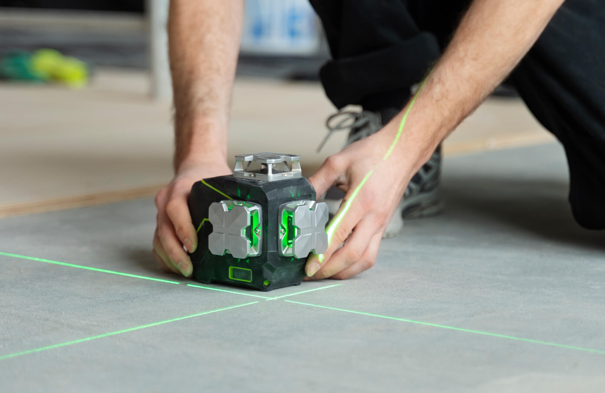 Installer using a green laser level to mark center lines on the subfloor before laying checkerboard tiles.