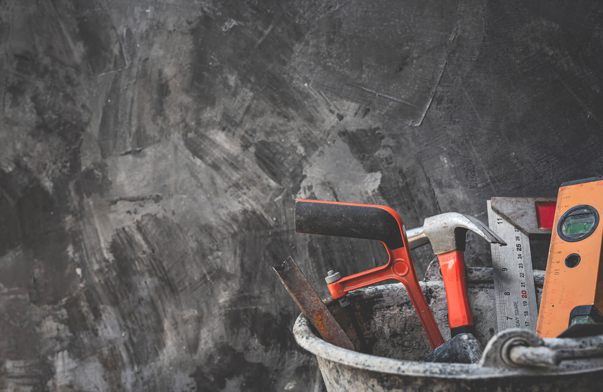 null Construction tools including a level and hammer in a bucket, ready for marble look tile installation work.