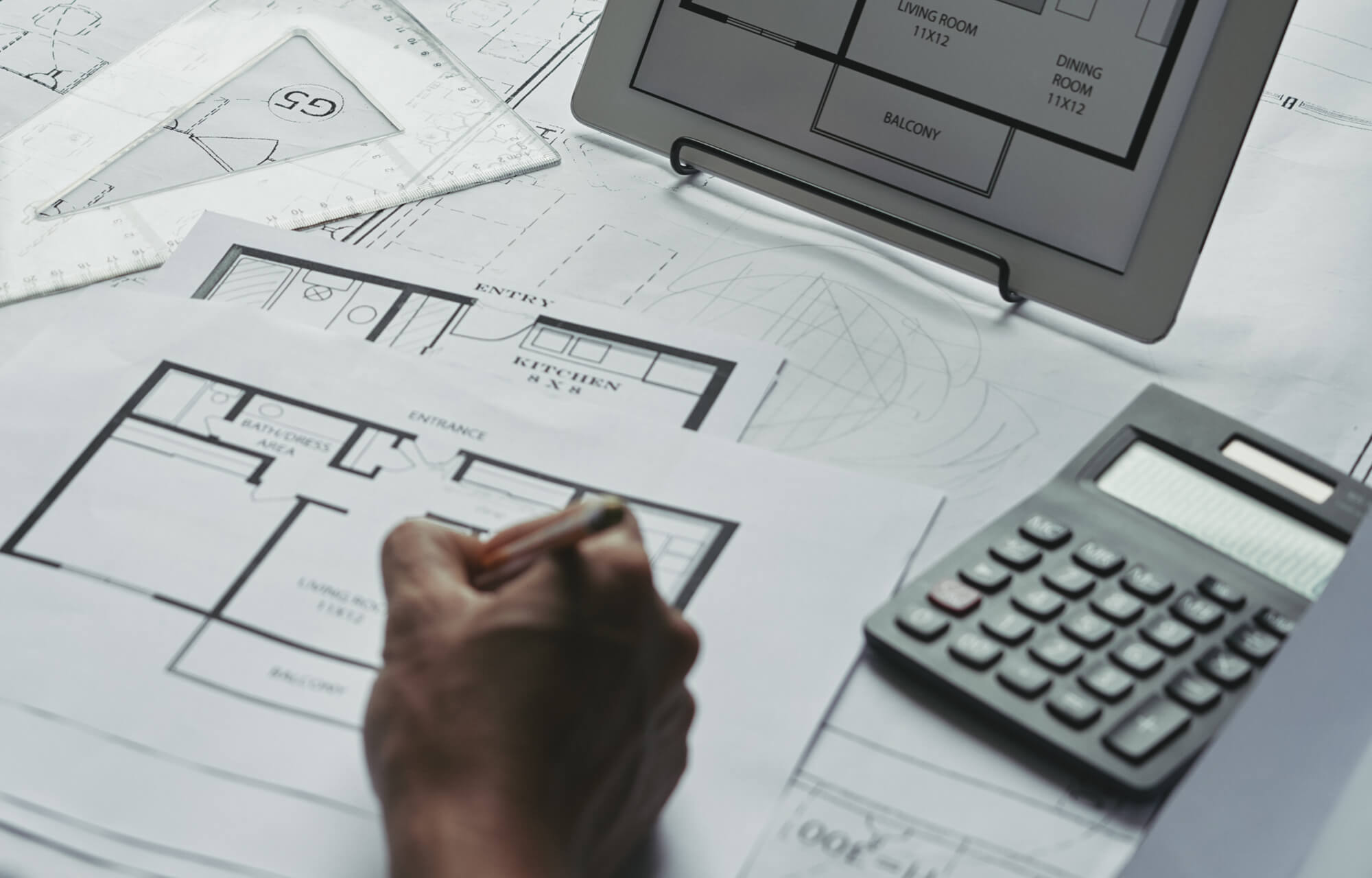 null Architect’s workspace featuring detailed floor plans, precise measuring tools, a calculator, and a digital tablet, capturing the meticulous process of designing a home with thoughtful spatial planning and lighting layout integration.