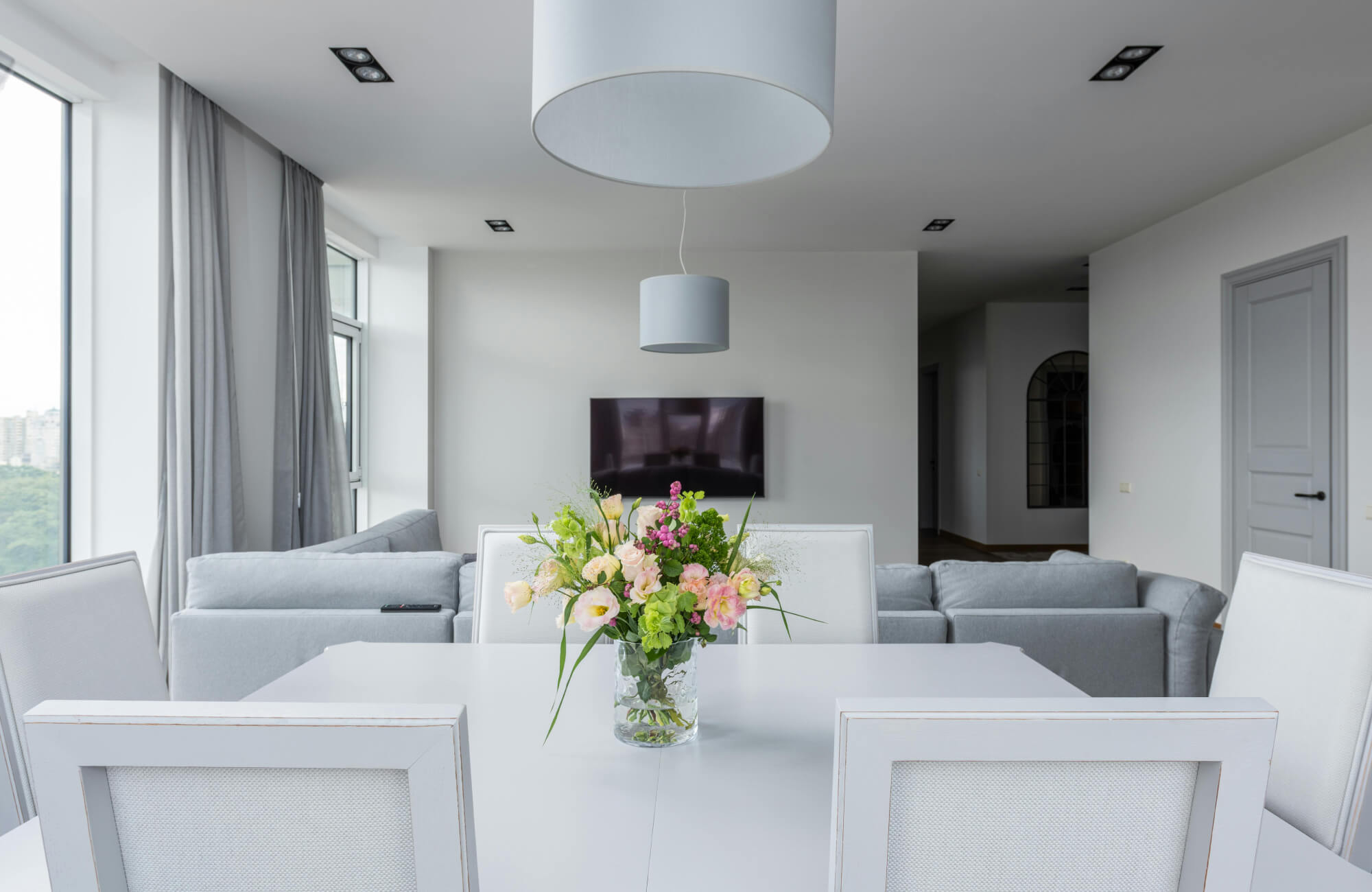 A minimalist dining area featuring a white table centered beneath a soft fabric pendant, supported by recessed lighting that adds balance without overpowering the space.