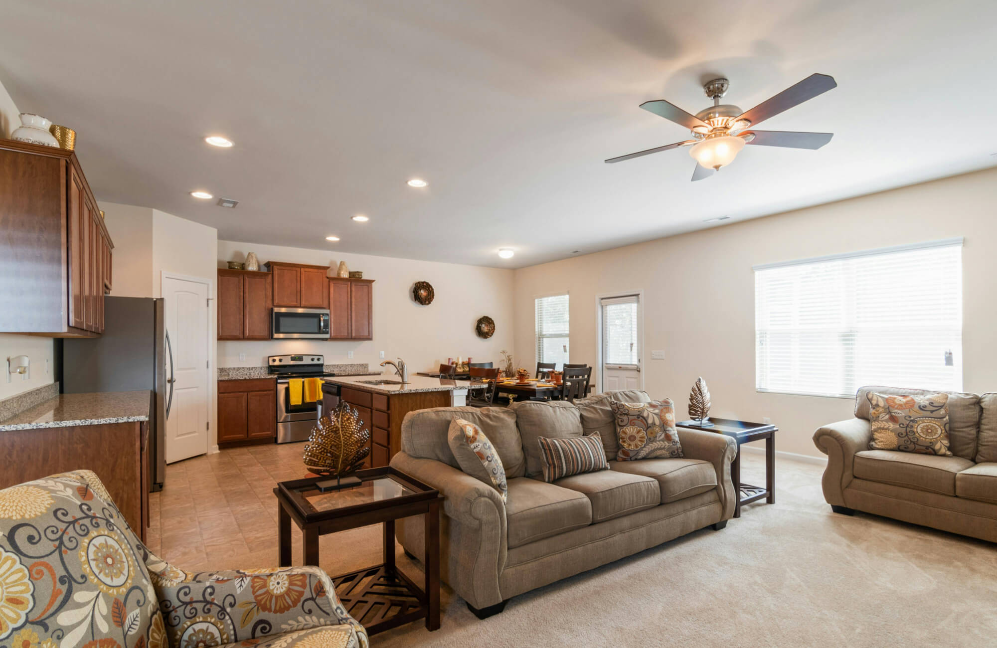 Open-plan layout with ceiling fan, recessed lighting, and natural light from large windows, connecting kitchen, dining, and living areas in a unified flow.
