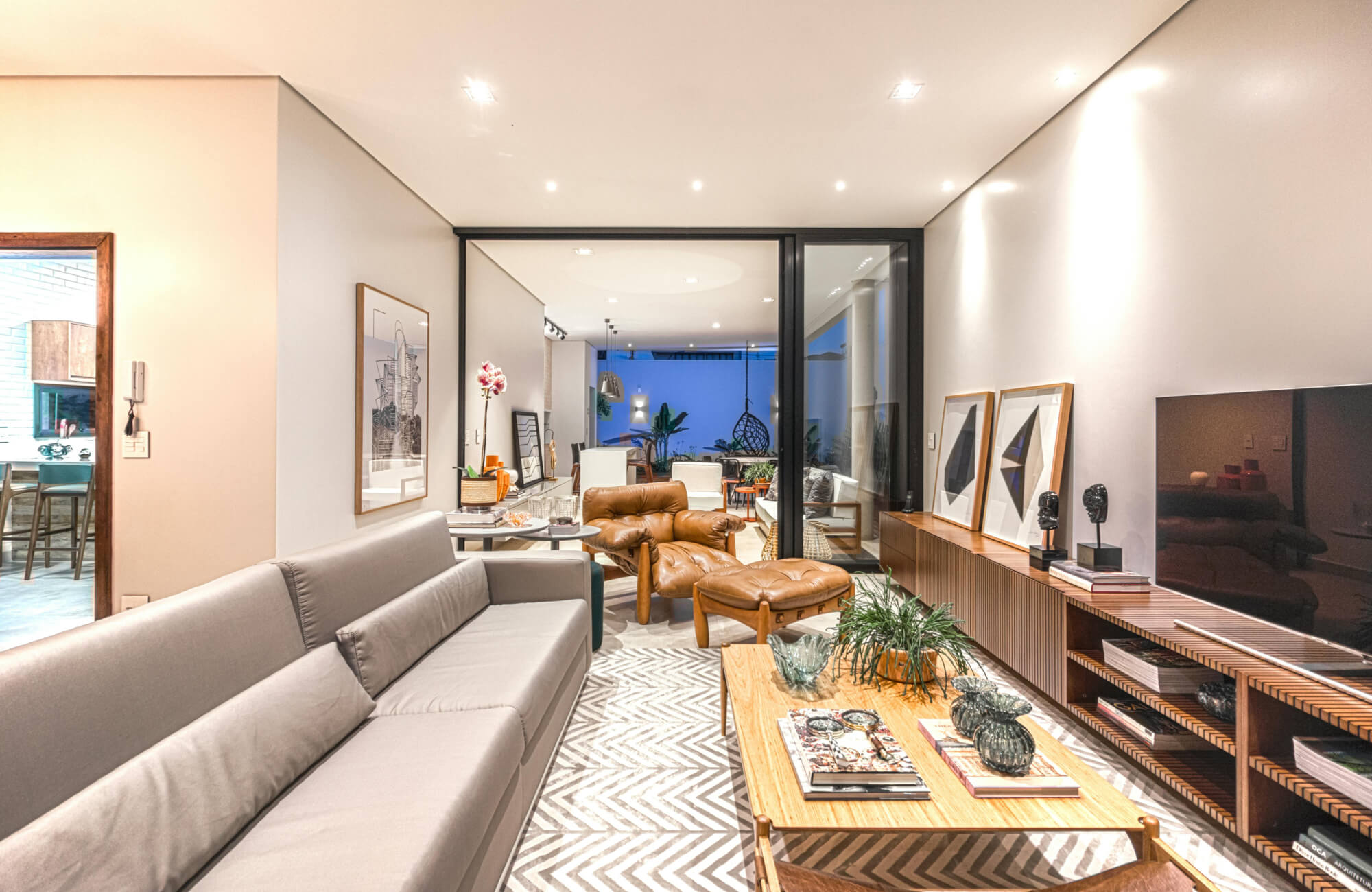 Contemporary space with spotlighting and ambient ceiling lights, connecting a cozy living room to a well-lit patio through sliding glass doors.