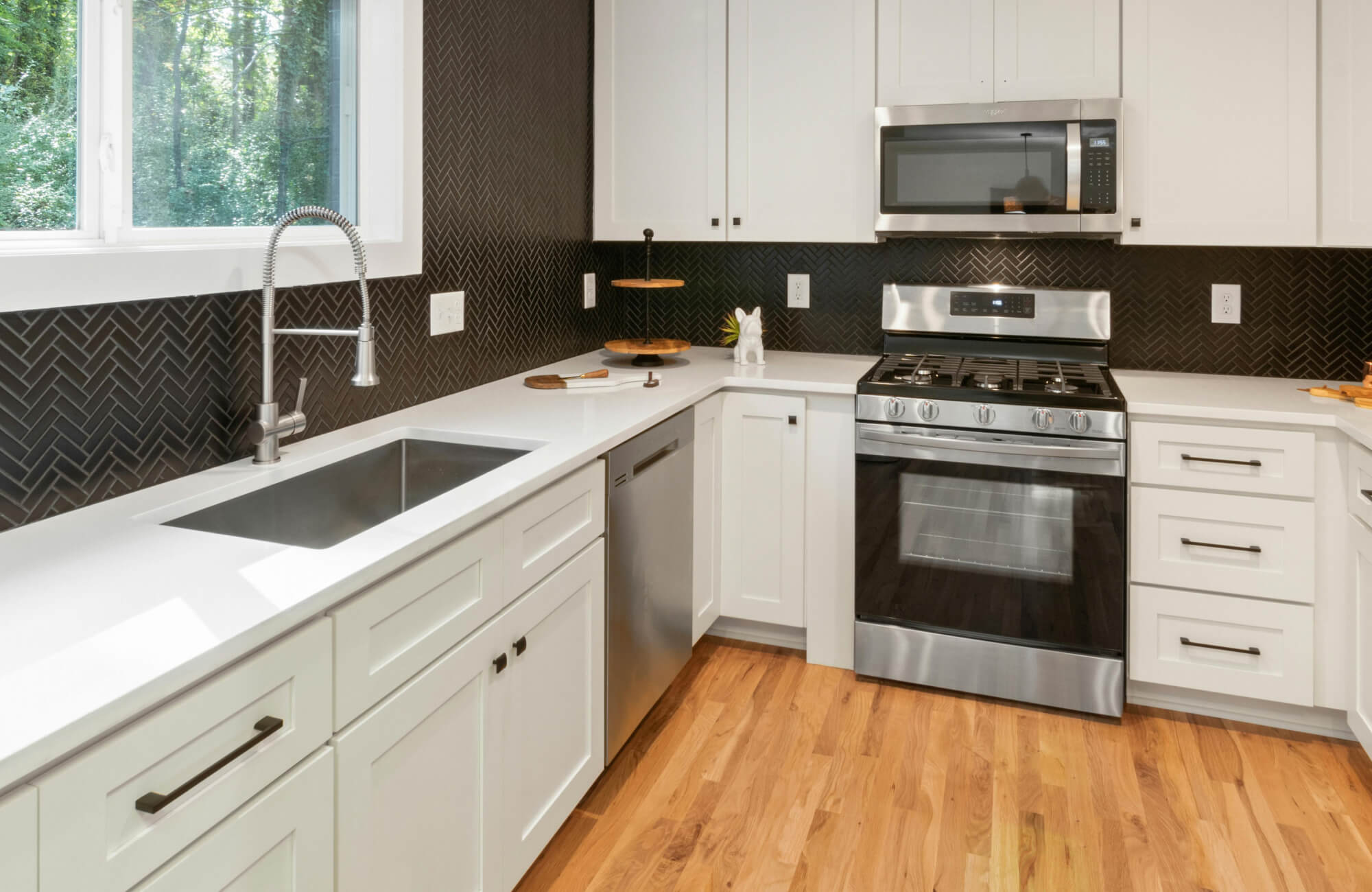 null Small modern kitchen featuring matte black backsplash tiles, light wood cabinets, and a clean white countertop with integrated sink and cooktop.