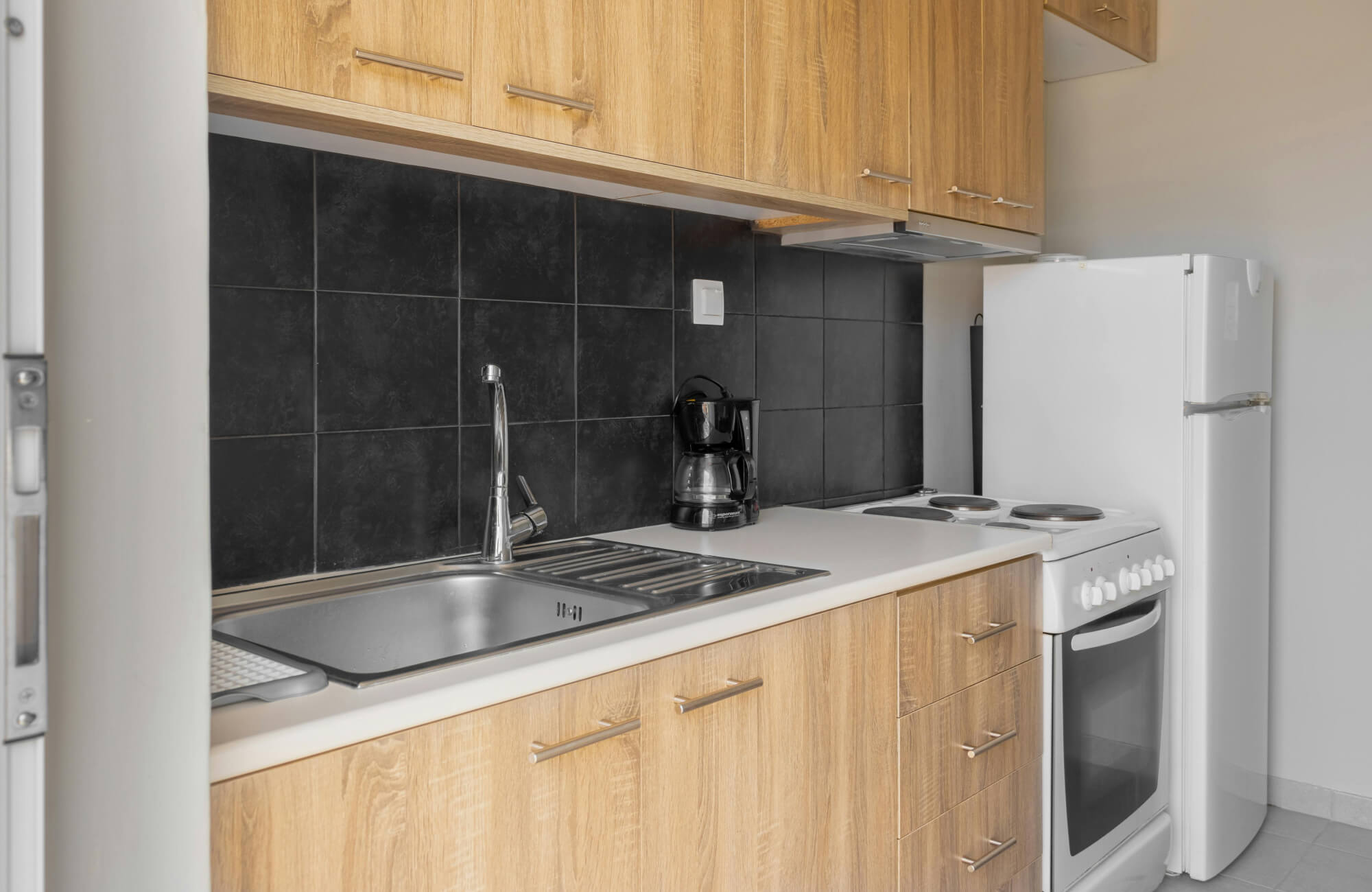 null Contemporary kitchen setup with matte black backsplash tiles, warm-toned wood cabinetry, and clean white appliances and surfaces.