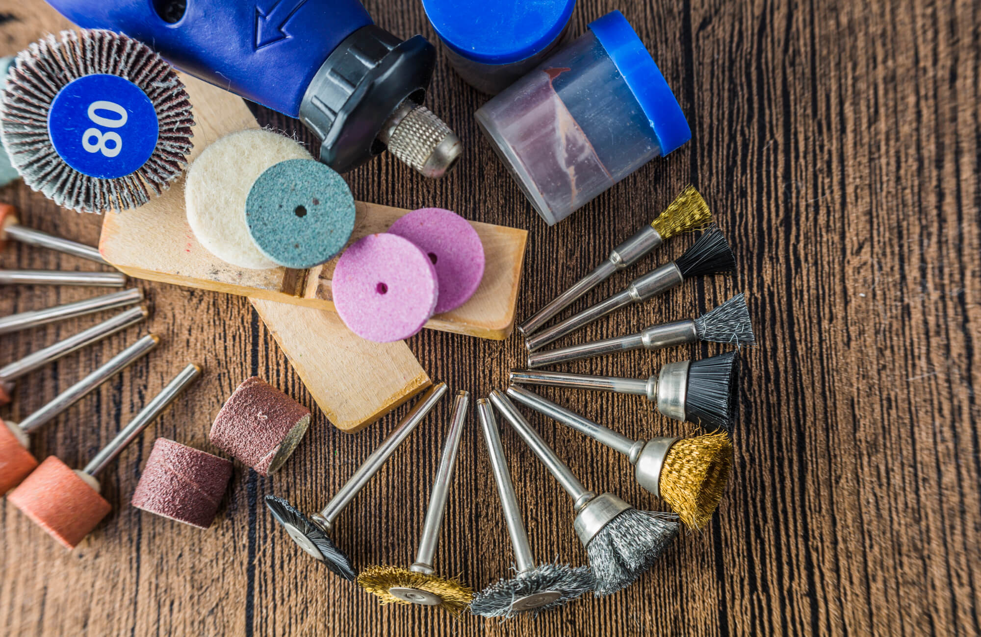 Close-up of assorted polishing tools, including wire brushes, felt discs, and sanding wheels, arranged on a rustic wooden surface for marble polishing.