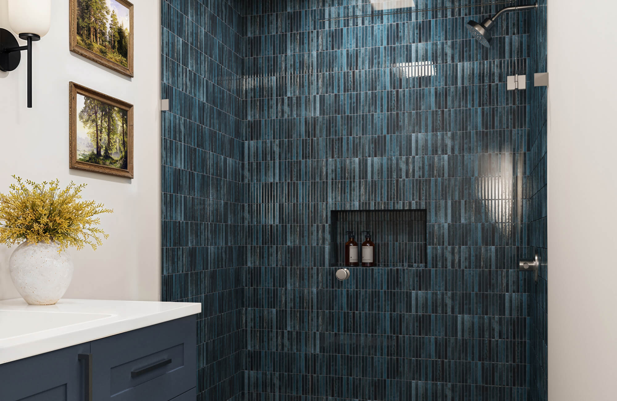 Stylish bathroom with glossy dark blue tiles, featuring a built-in shower shelf, framed artwork, and a vase on the vanity.