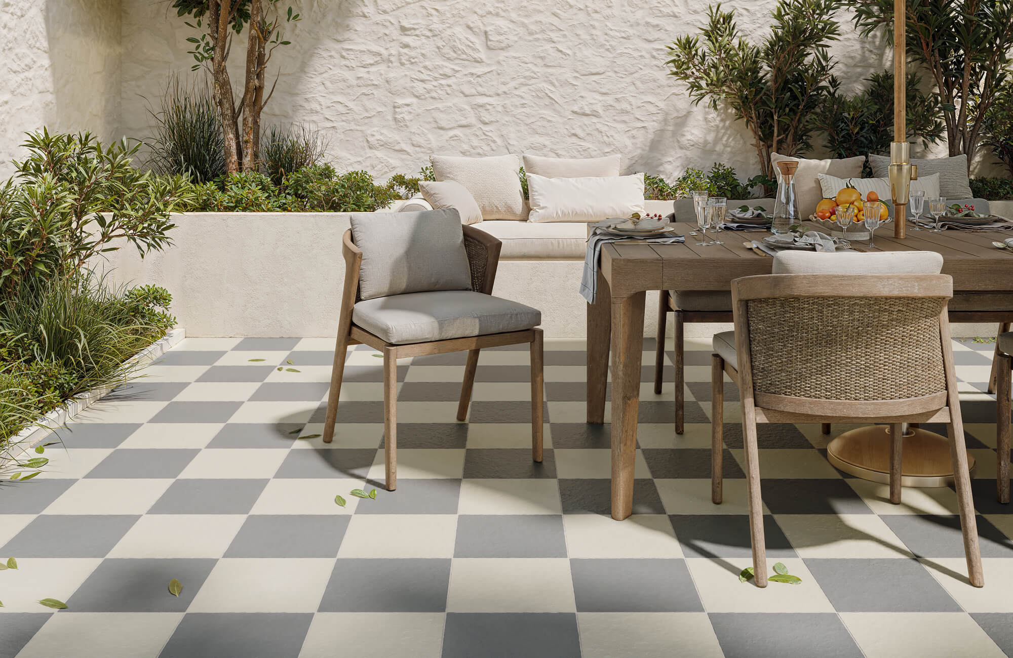 null Outdoor dining area featuring neutral checkerboard floor tiles in soft gray and ivory, paired with natural wood furniture and lush garden accents.