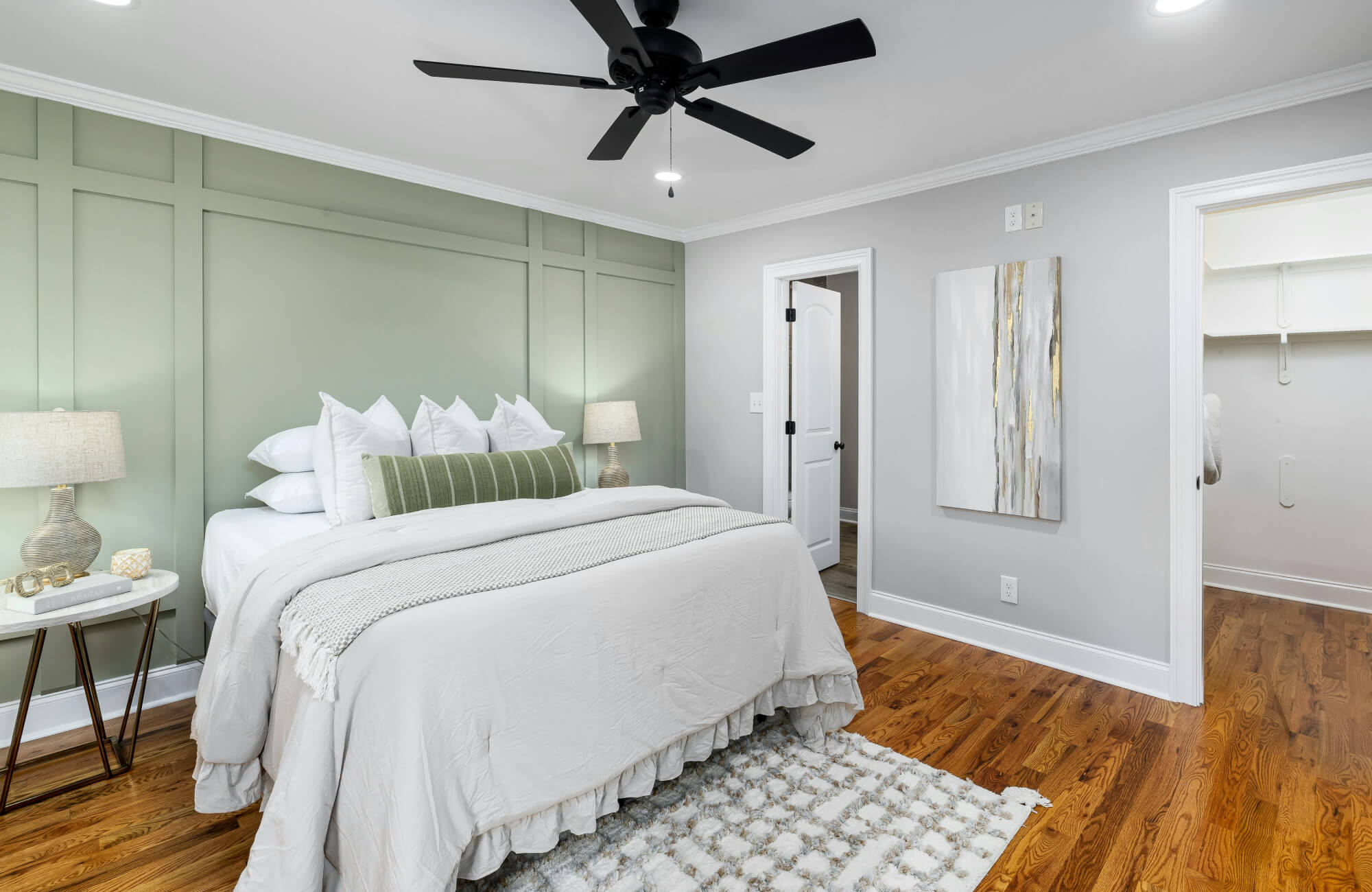 null Minimal bedroom with white bedding, layered pillows, a green striped bolster pillow, and a sage green paneled accent wall behind the bed.
