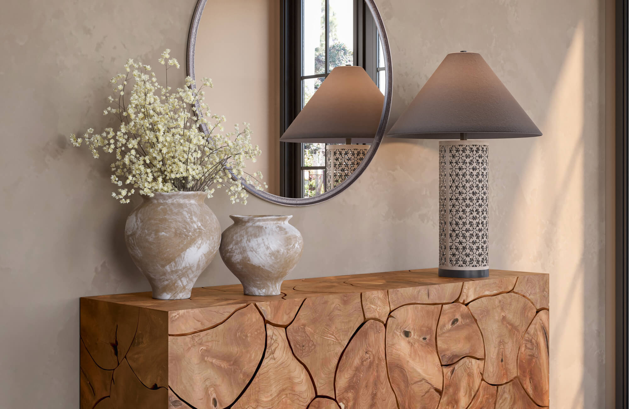 Pair of textured neutral ceramic vases with delicate white branches styled on a carved wood console beside a patterned table lamp and round wall mirror.