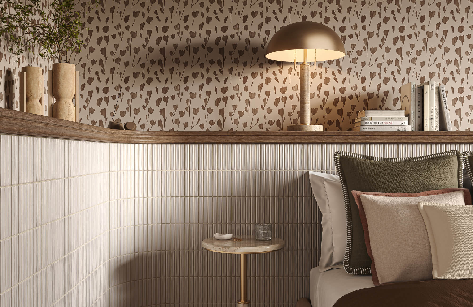 Long bedroom ledge styled with travertine vases, books, a sculptural lamp, and greenery against floral wallpaper and vertically stacked cream tile.