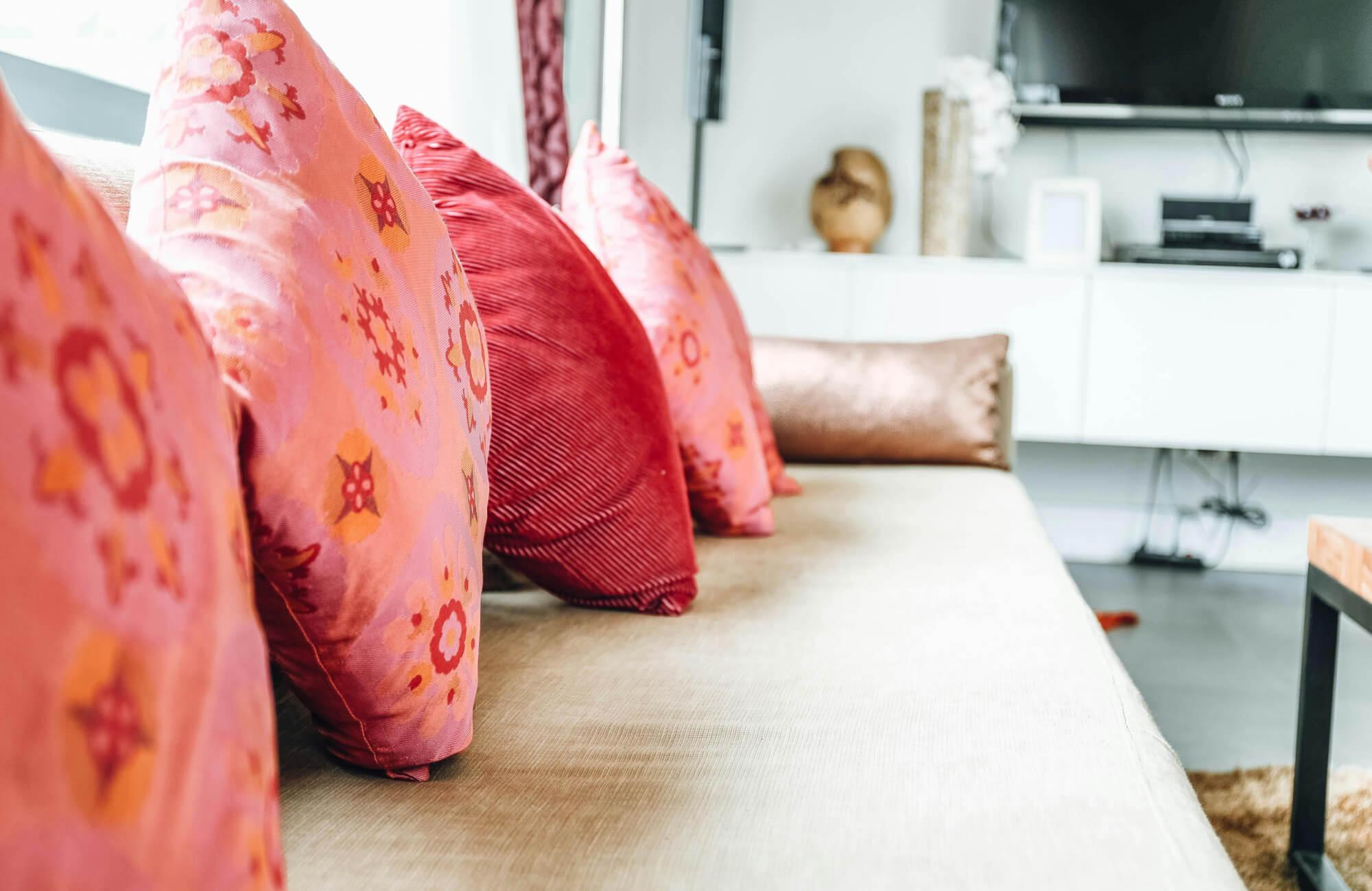 null Bright eclectic living room with coral pink floral throw pillows on a beige sofa, white media console, and playful modern accents.