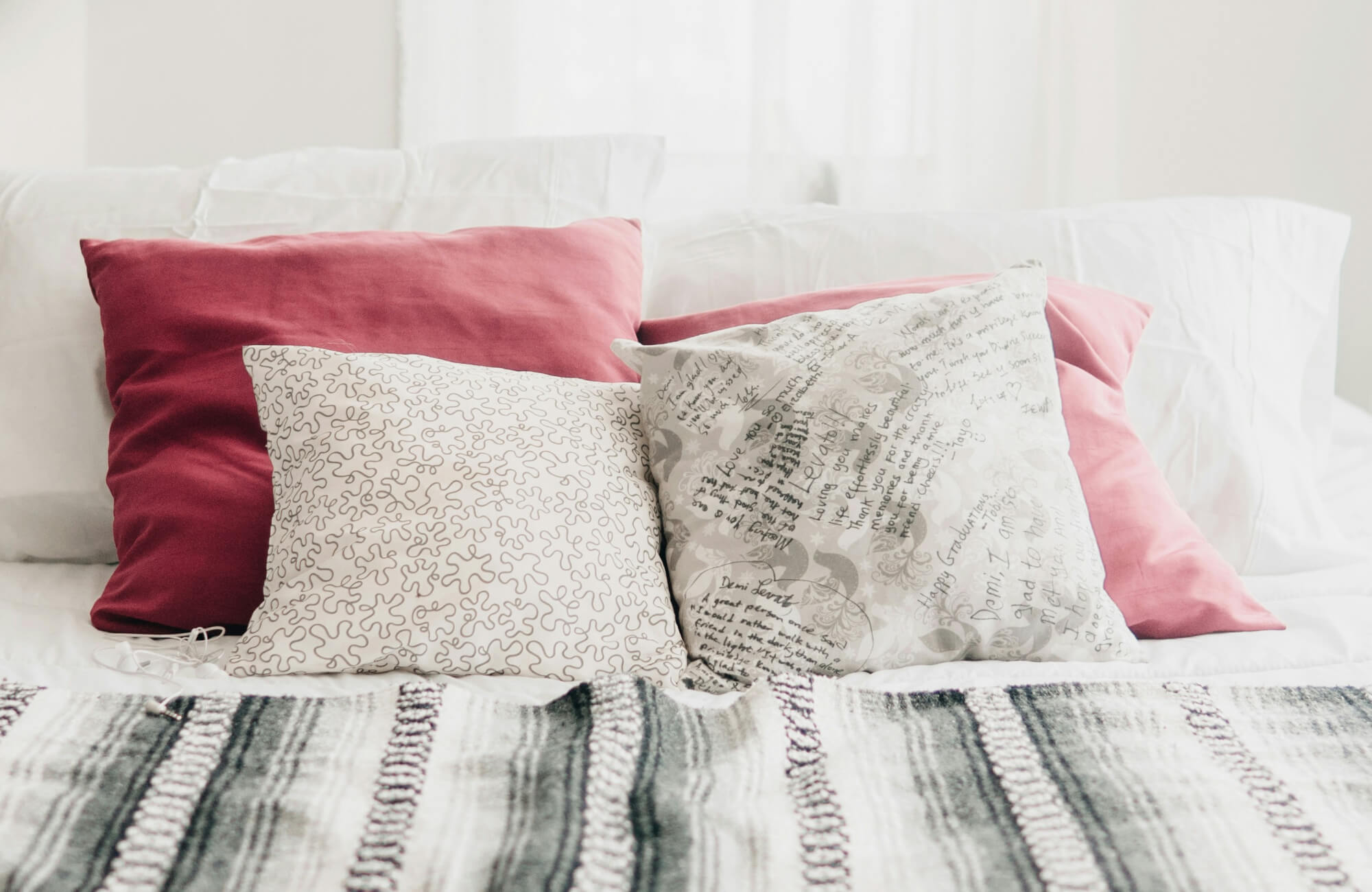 null Soft modern bedroom with blush pink and script-patterned throw pillows on white bedding, layered with a cozy striped throw.