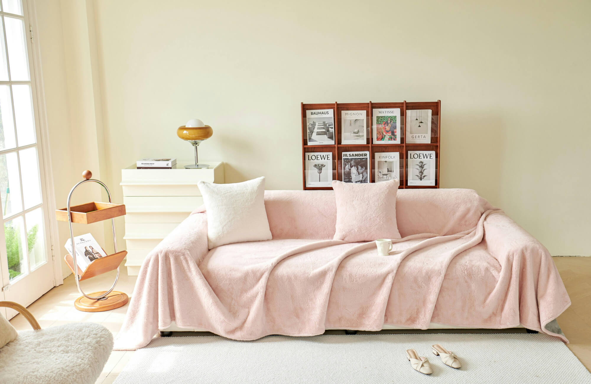 null Soft eclectic living room with blush sofa cover, cream and pink throw pillows, magazine rack, and sunlit pastel decor.
