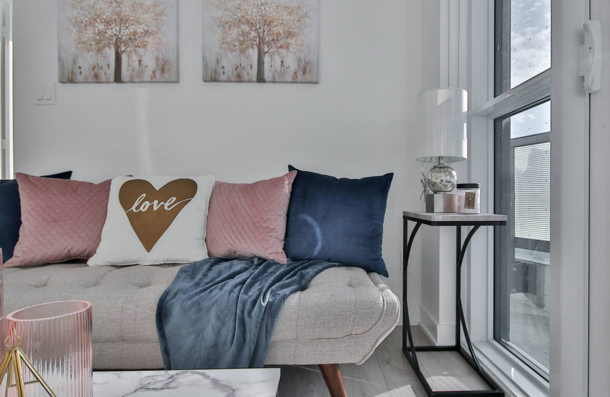 null Modern glam living room with blush pink and blue throw pillows, love accent cushion, gray daybed, and bright window light.