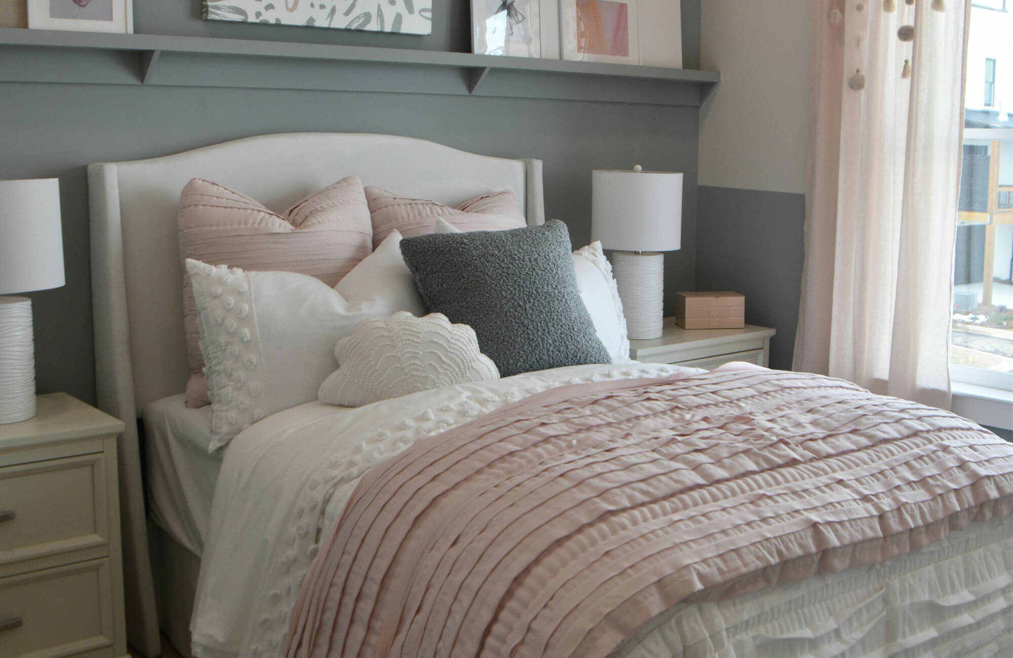 null Soft modern bedroom with blush pleated bedding, white and light pink textured throw pillows, gray accent wall, and airy window light.
