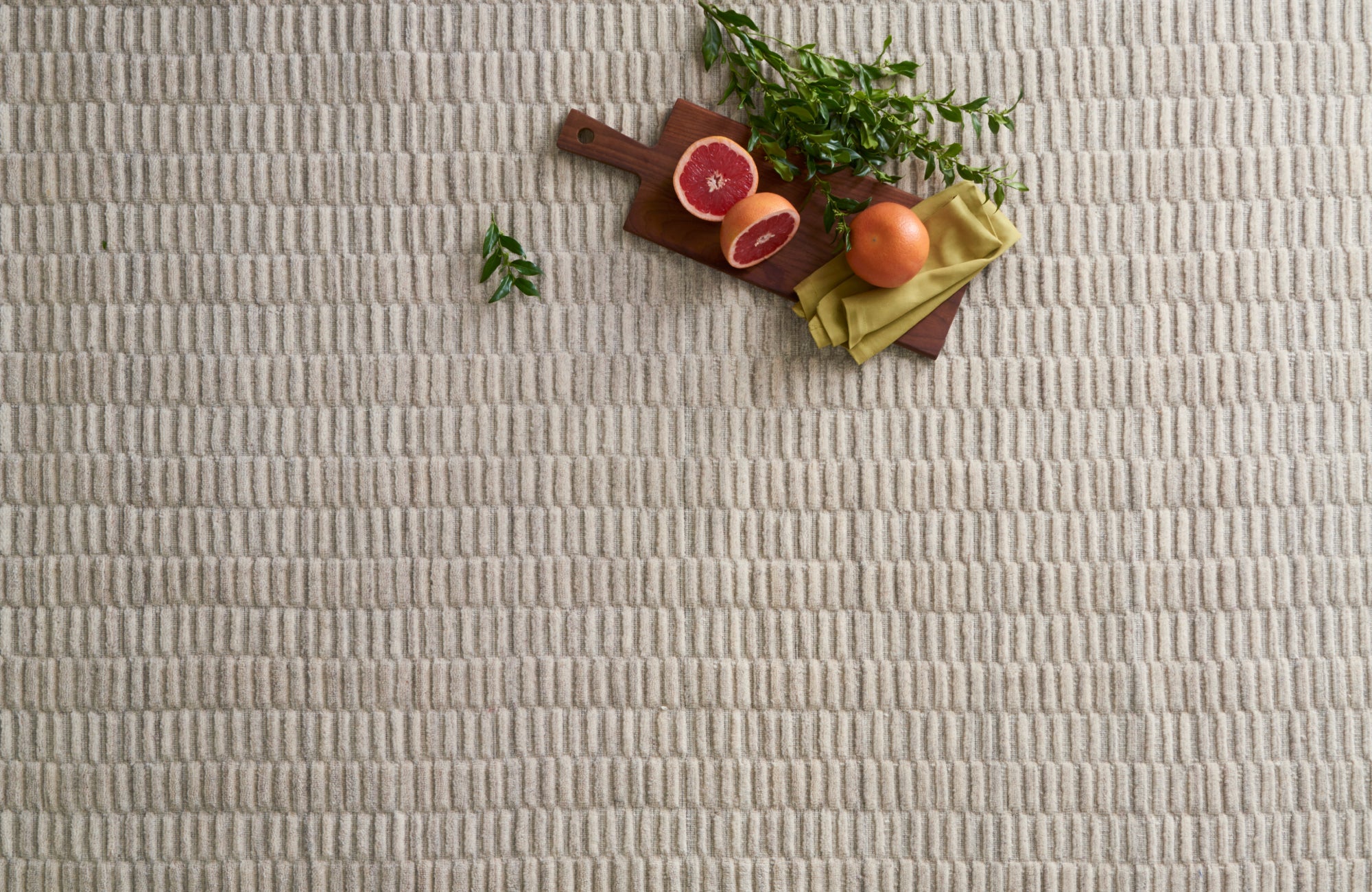 null Overhead view of a textured neutral rug with fruit and herbs, showcasing indoor decor and tactile surface detail.