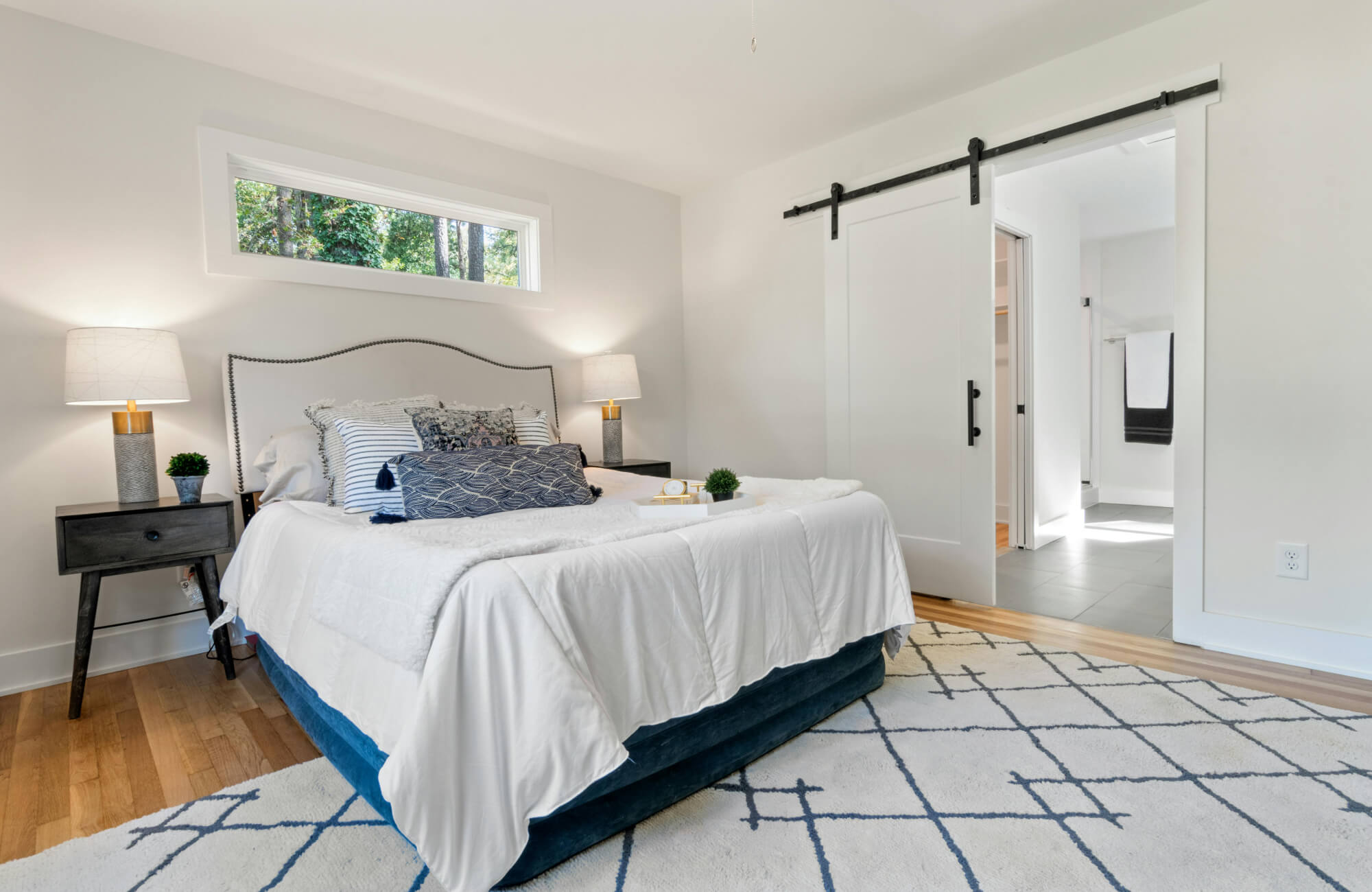 null A cozy bedroom featuring a light upholstered bed, warm wood flooring, simple nightstands, and a geometric rug that adds gentle contrast to the clean, airy layout.